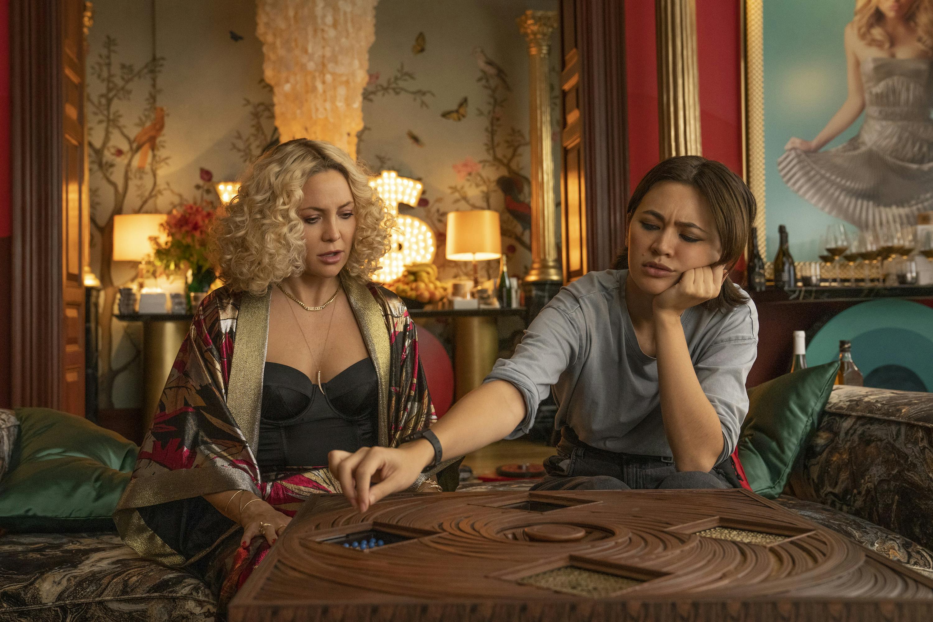 Birdie Jay (Kate Hudson) and Peg (Jessica Henwick) work there way through a wooden puzzle invitation.