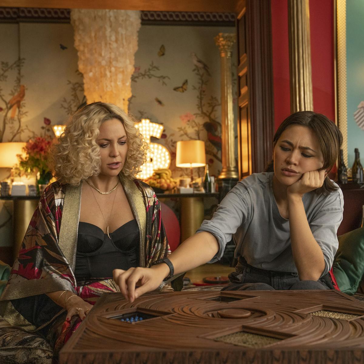 Birdie Jay (Kate Hudson) and Peg (Jessica Henwick) work there way through a wooden puzzle invitation.