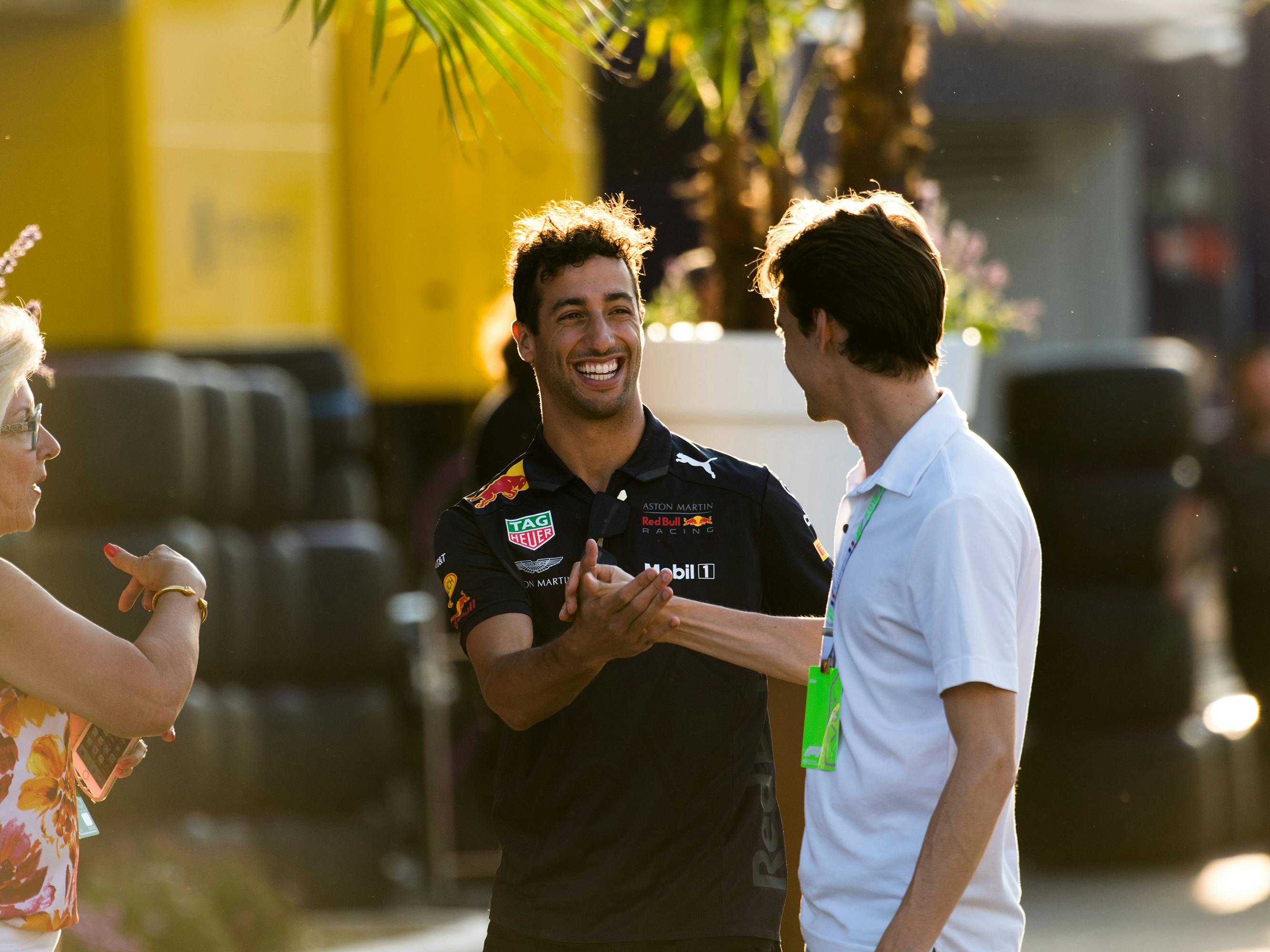 Driver Daniel Ricciardo smiles and shakes hands with a fan in the paddock.