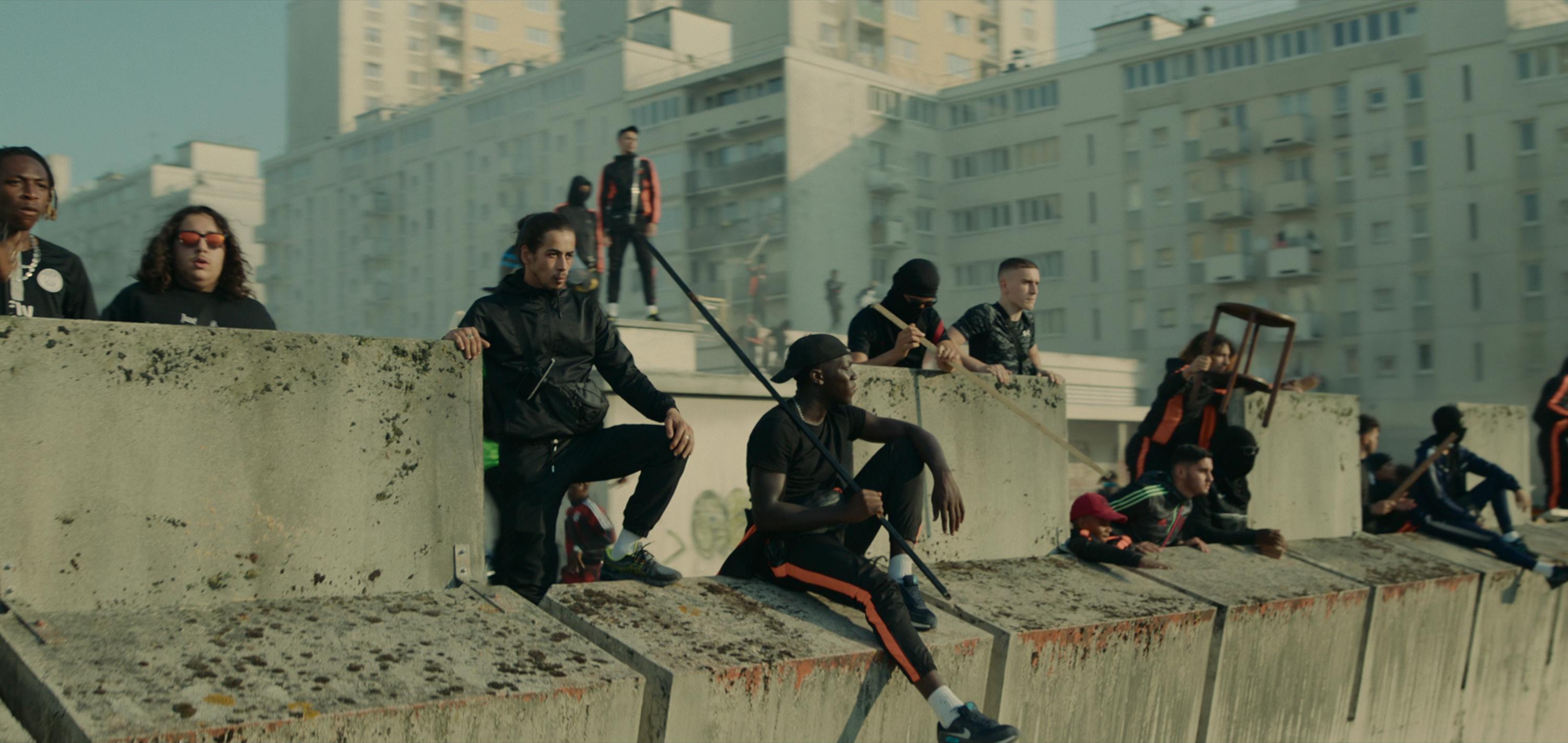 The cast and crew of Athena sit on a cement wall. 