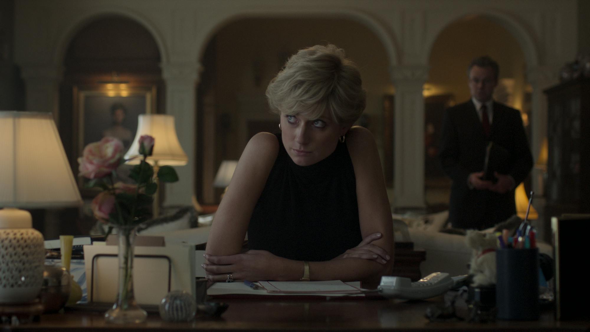 Princess Diana (Elizabeth Debicki) wears a sleeveless black shirt and hunches over her desk.