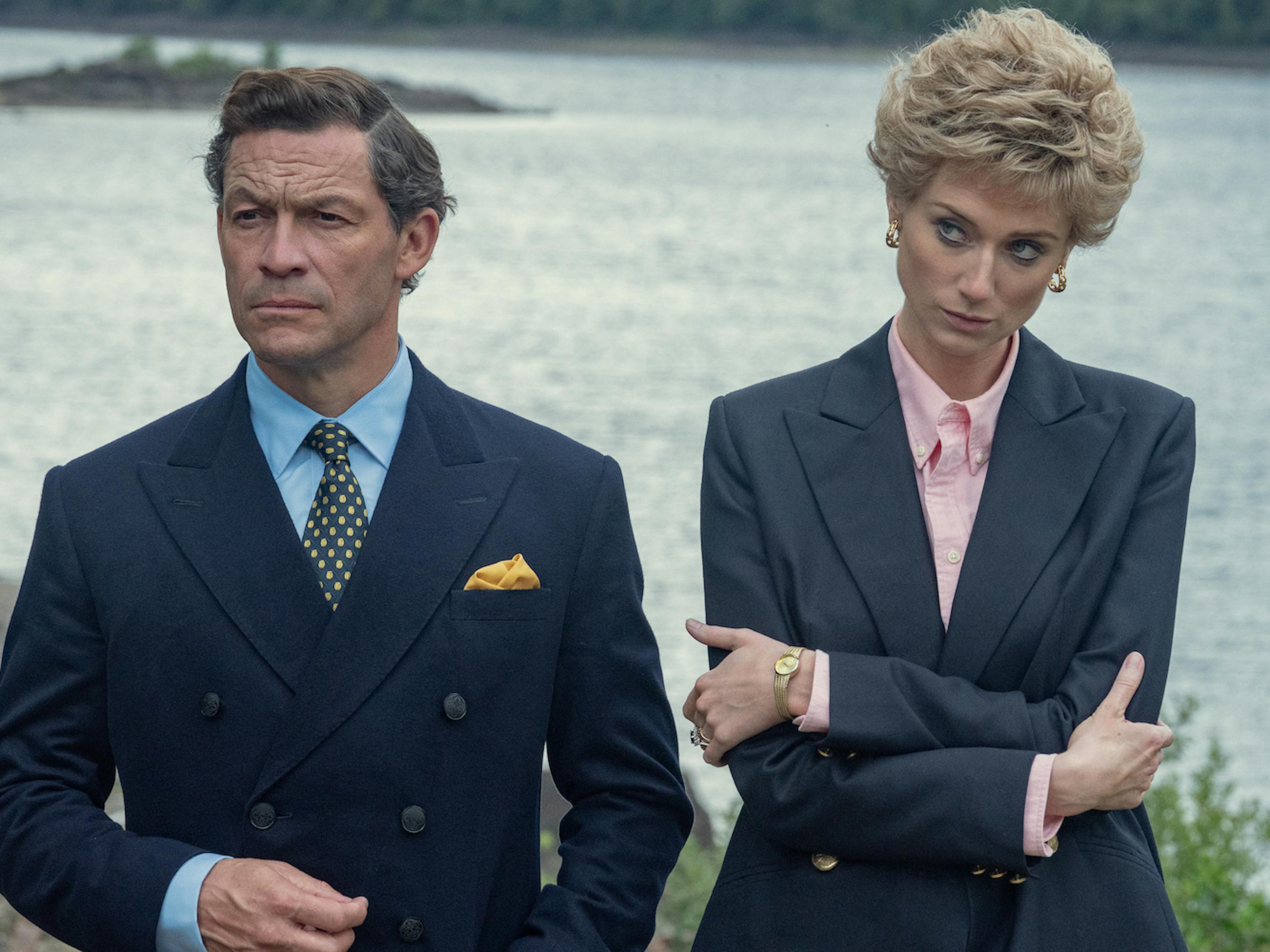 Prince Charles (Dominic West) and Princess Diana (Elizabeth Debicki) wear navy blazers and stand by some water.