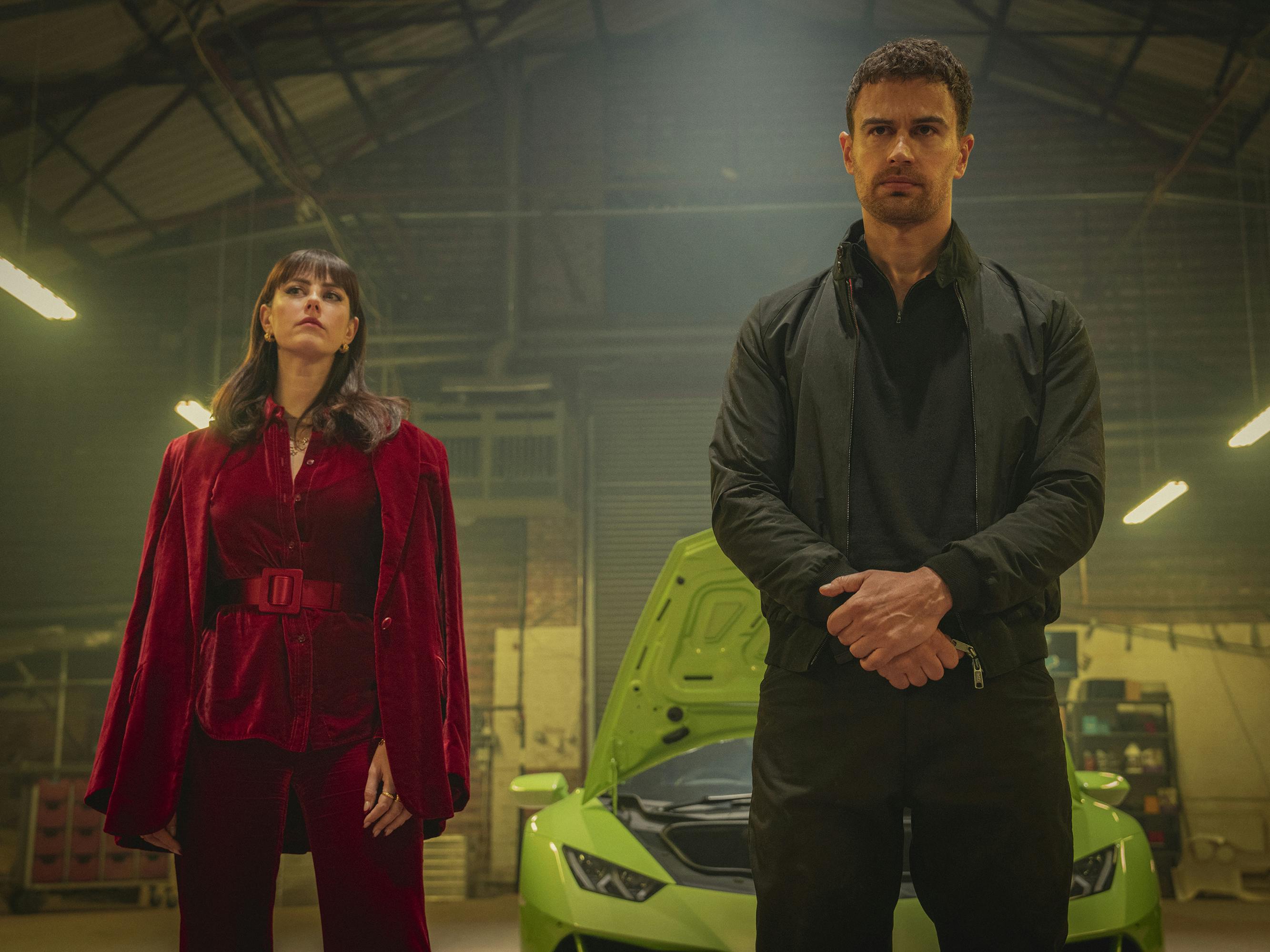 Susie Glass (Kaya Scodelario) and Eddie Horniman (Theo James) stand together in a warehouse. Behind them is a lime green car.