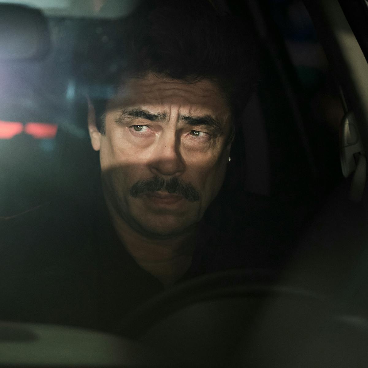 Tom Nichols (Benicio del Toro) frowns in a darkened car.