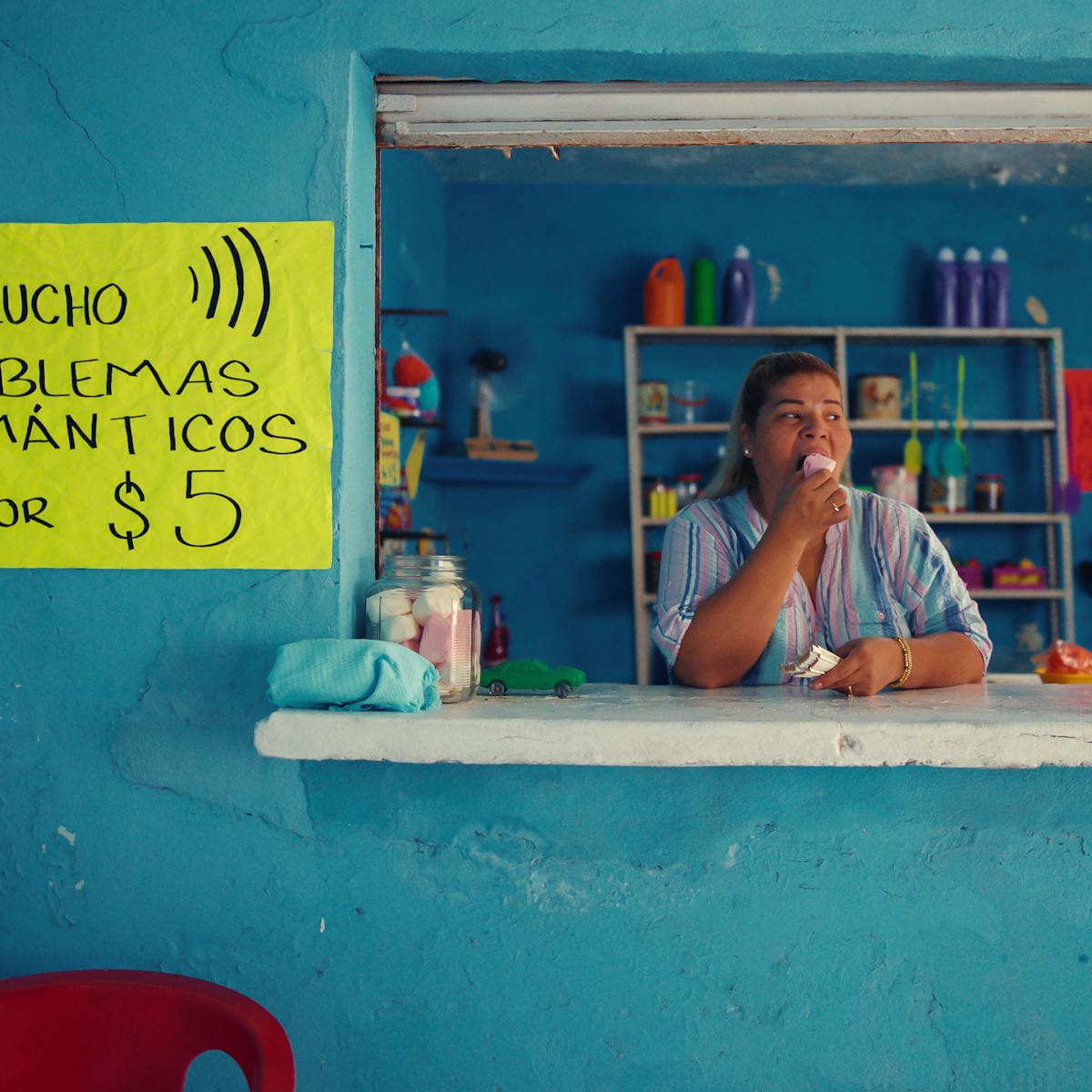 Los (casi) Idolos de Bahia Colorada character eats an ice cream in a blue cafe service window.