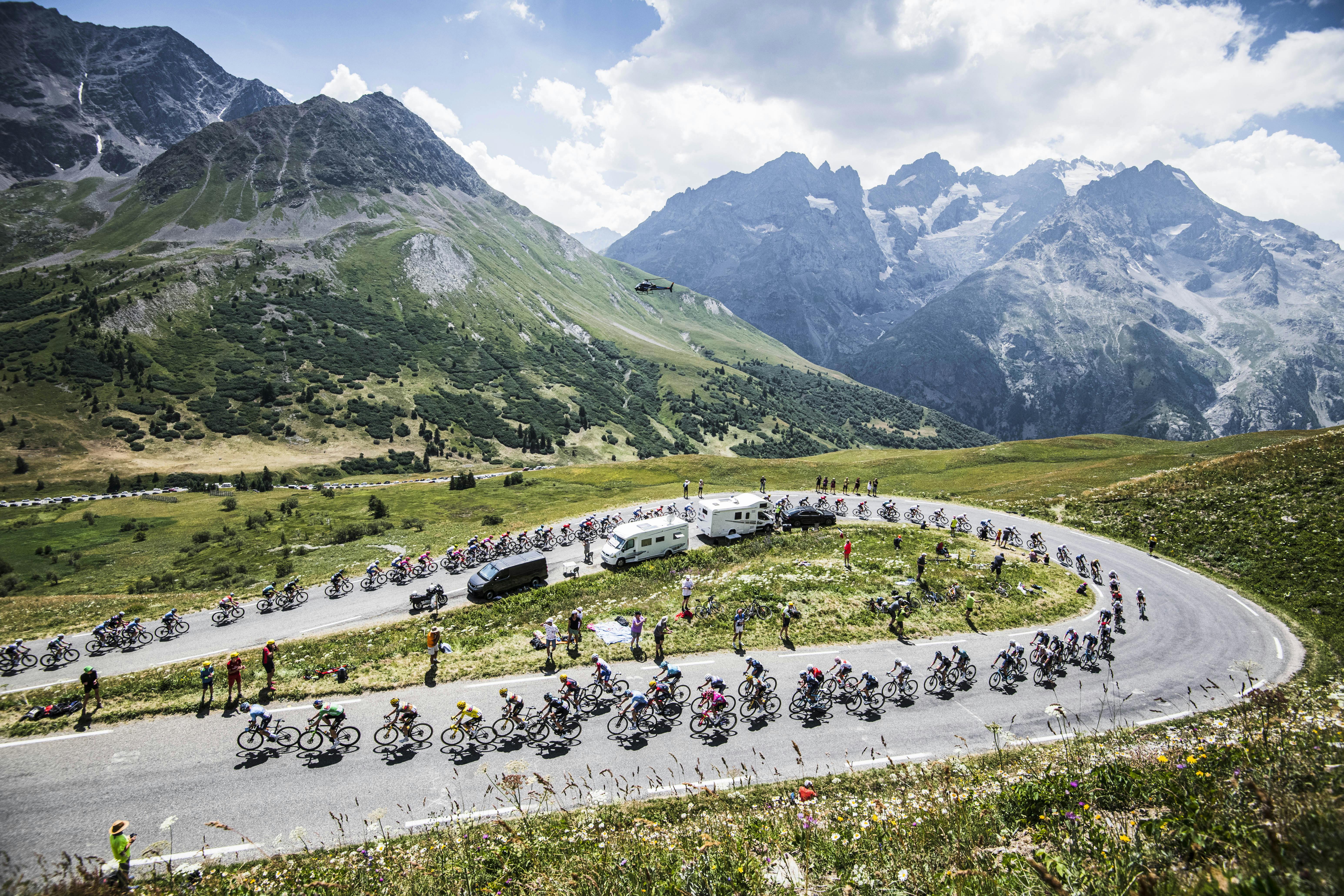 A gorgeous uphill section of the Tour de France, backgrounded by snow-capped mountains.