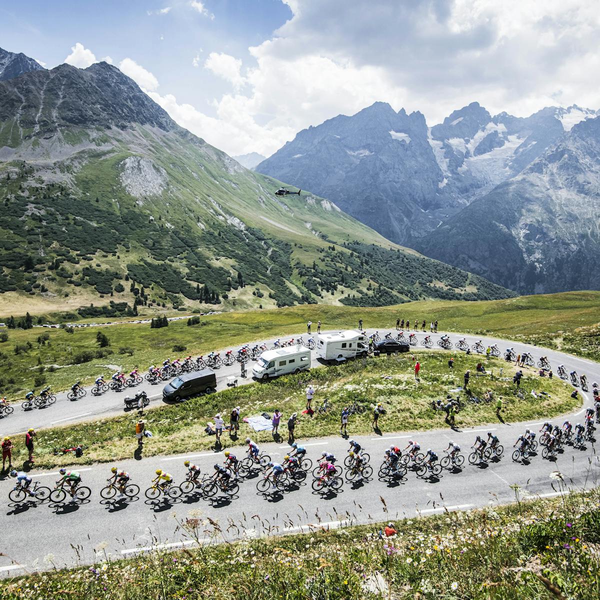 A gorgeous uphill section of the Tour de France, backgrounded by snow-capped mountains.