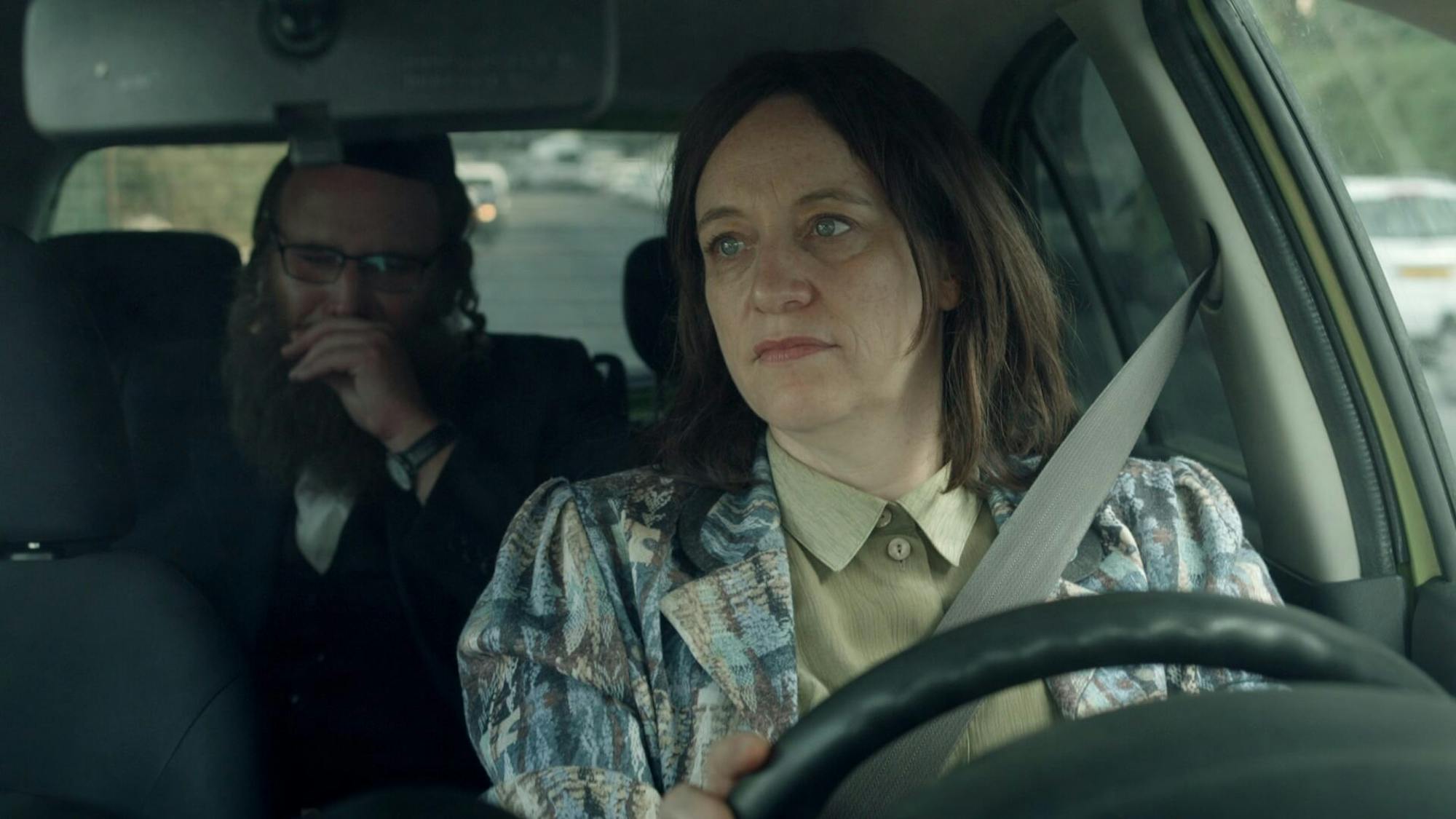 Tovi Shtisel (Eliana Shechter) sits in the front seat of the car, and Zvi Arye Shtisel (Sarel Piterman) sits in the back looking concerned.