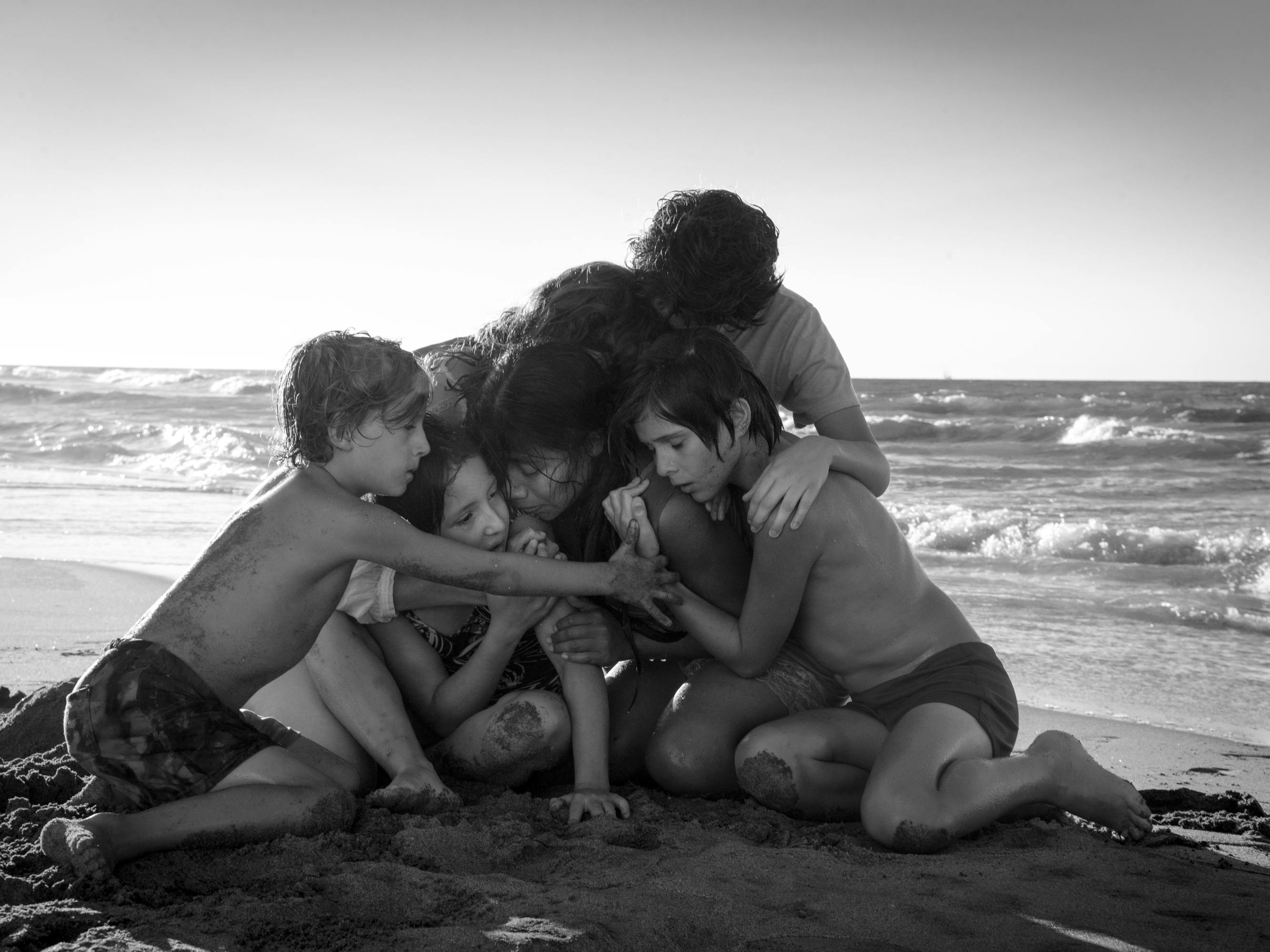 Six children hug in a cluster on a sandy beach.