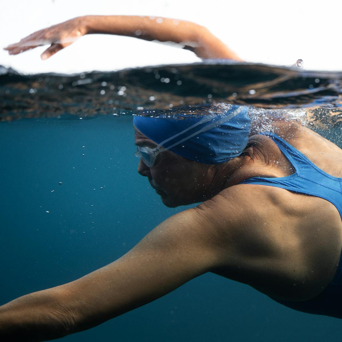 Diana Nyad (Annette Bening) swims through the water in a navy and light blue bathing suit, and matching blue swim cap.