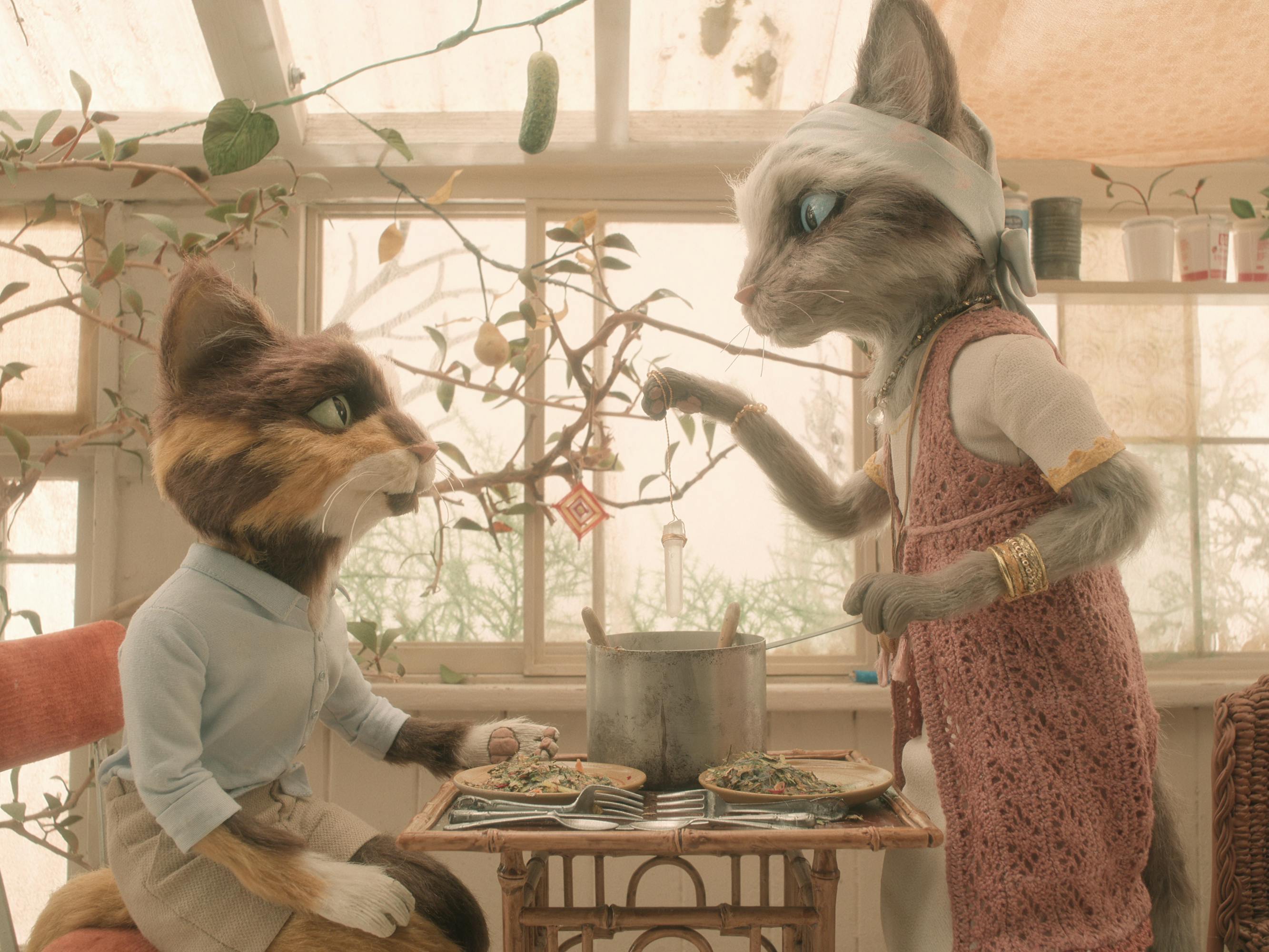 To furry creatures talk together over a pot of soup. One wears a blue shirt and khakis and the other wears a red dress and white headband.