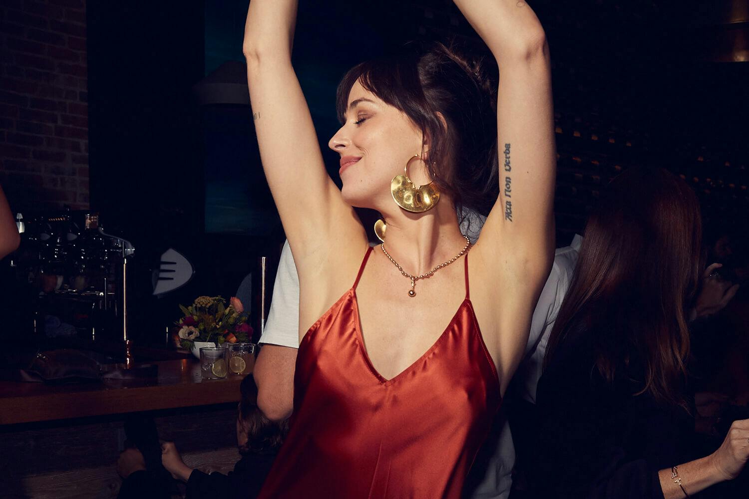 Dakota Johnson dancing with her hands in the air while wearing a red silk slip dress at the Telluride Film Festival, 2021.