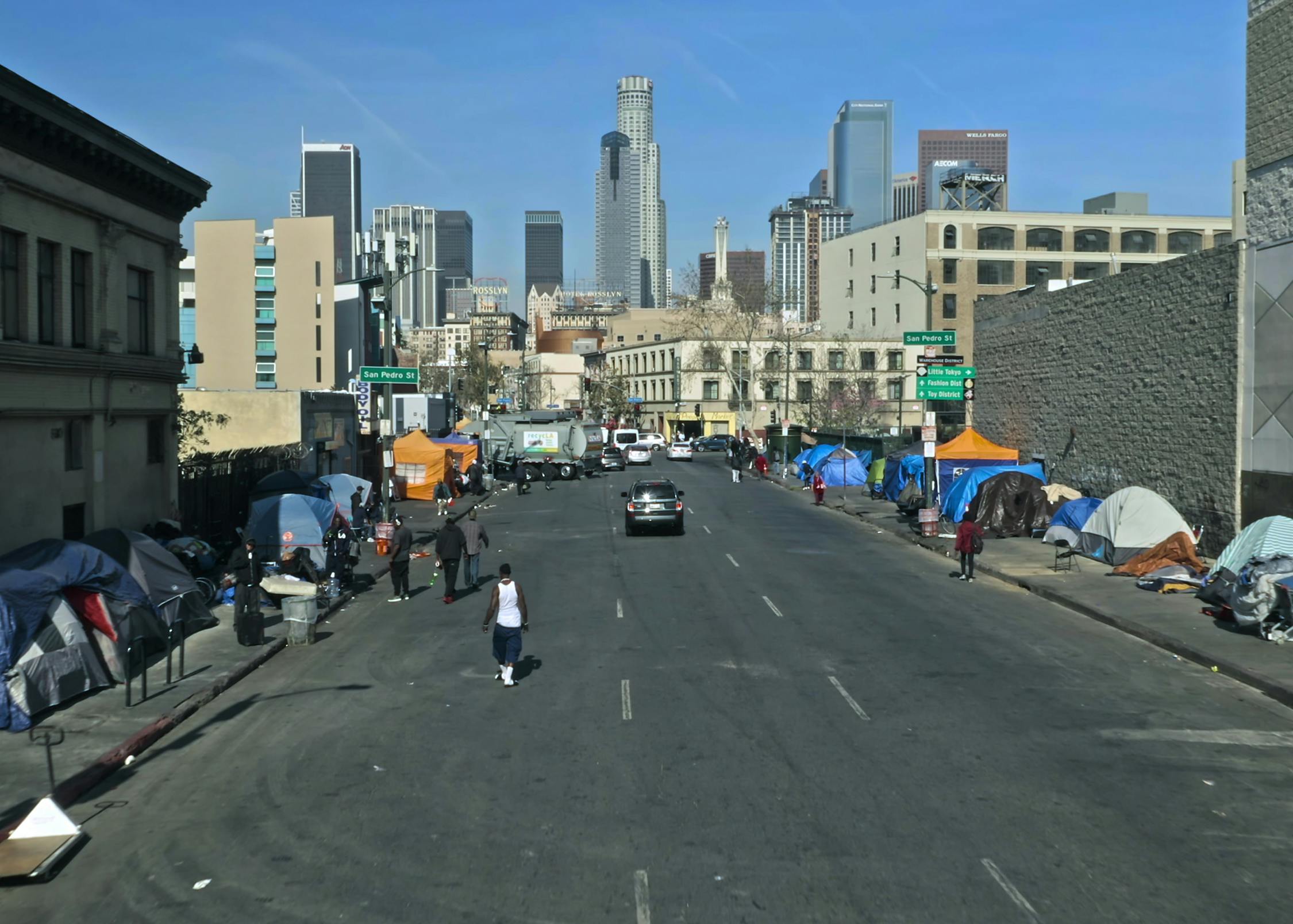 A street lined with multi-colored tents. In the background are buildings, street signs, and cars.