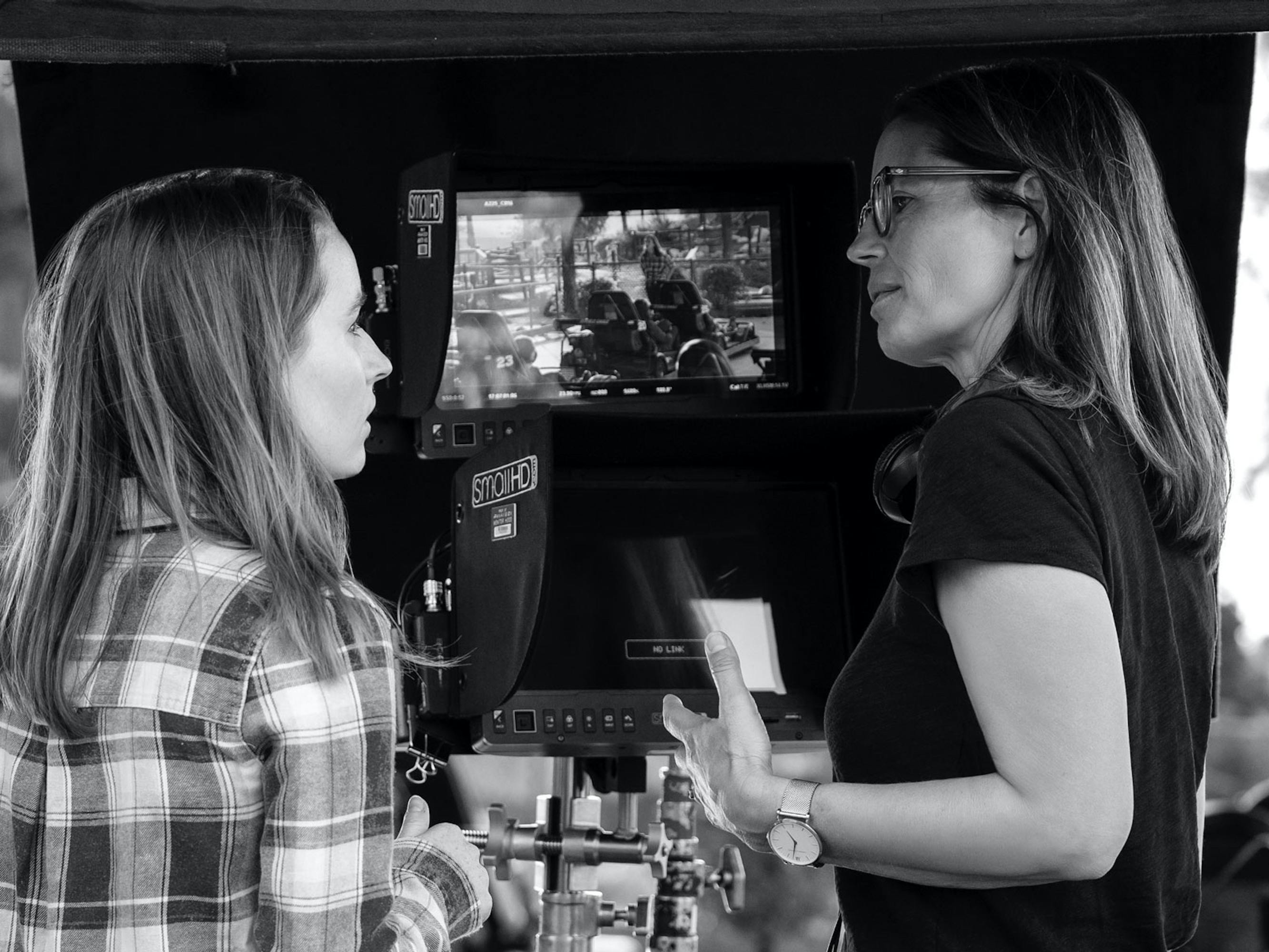 Kaitlyn Dever and Susannah Grant stand beside camera gear in this black-and-white shot.
