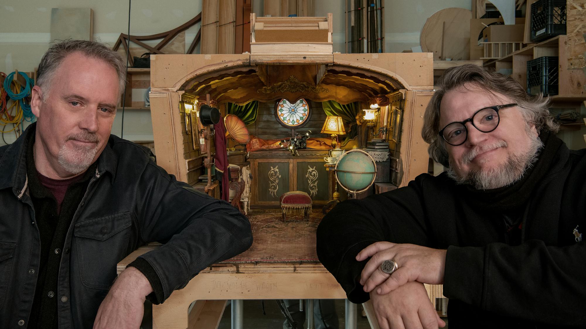 Mark Gustafson and Guillermo del Toro pose next to a miniature set, wearing black jackets.