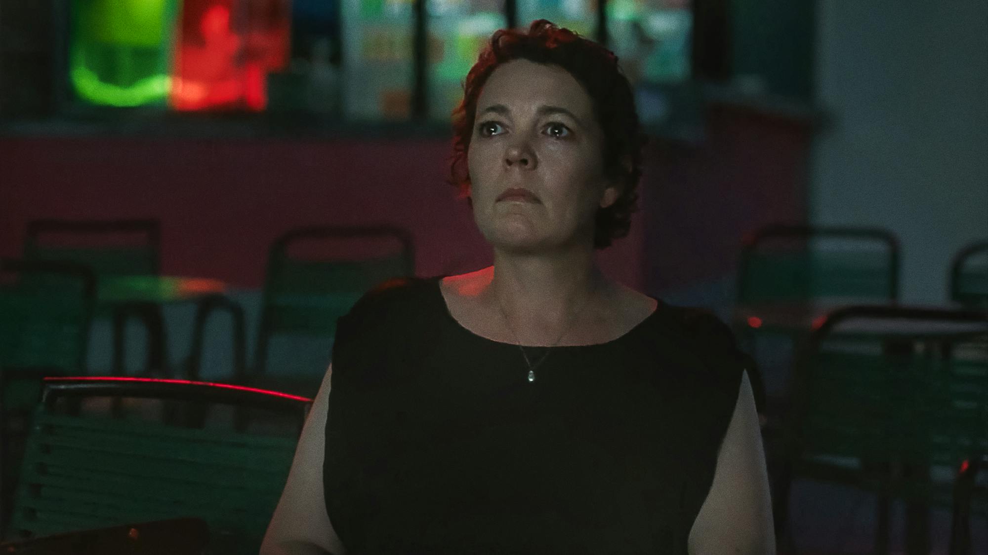 Olivia Colman wears a black dress in an empty, dark movie theater.