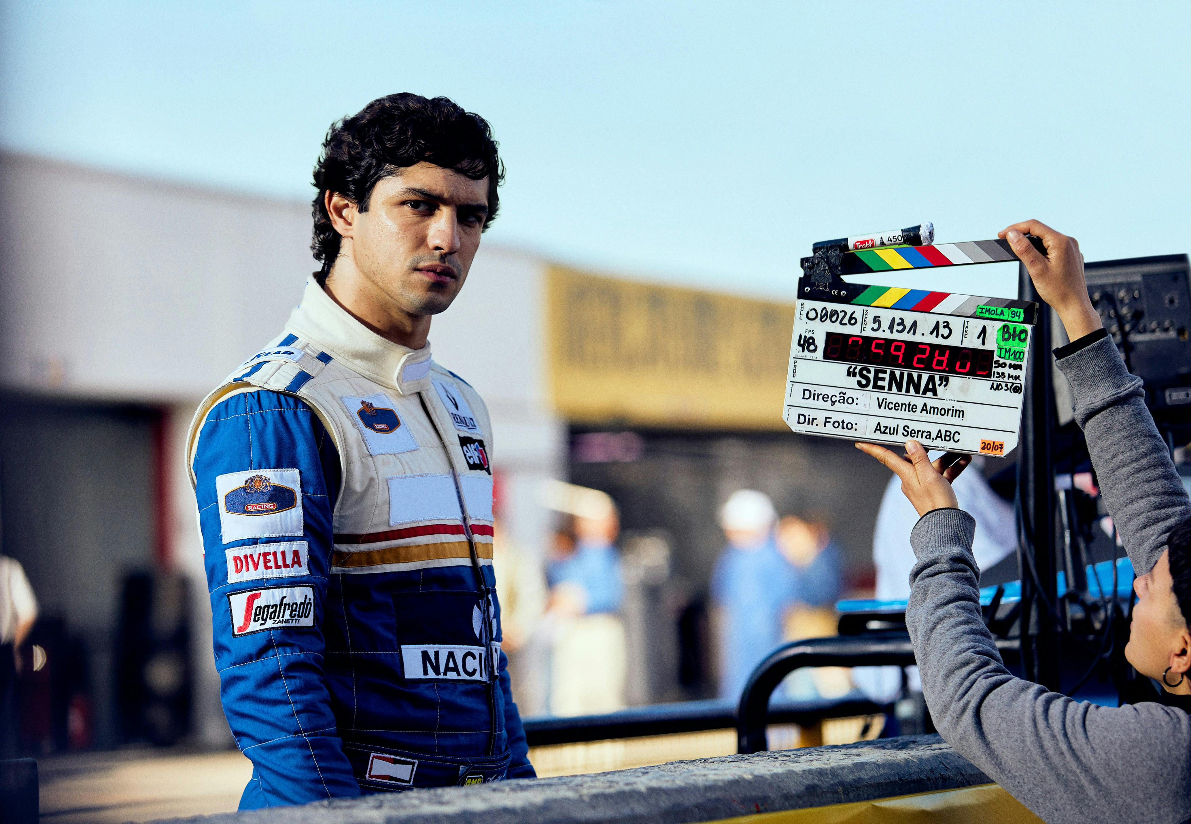 Ayrton Senna (Gabriel Leone) wears a white and blue racing suit behind the scenes of Senna.