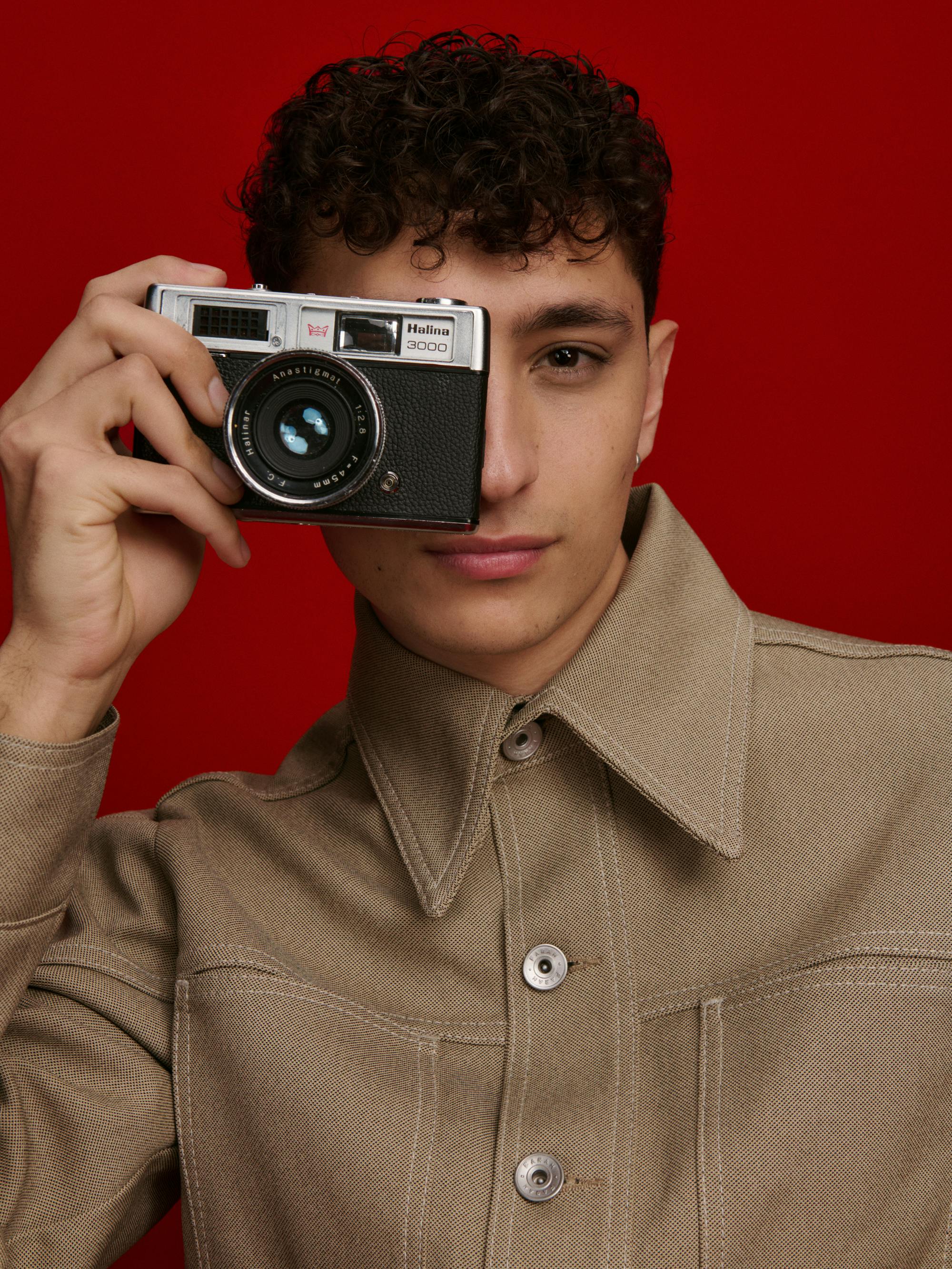 Jayden Revri wears a khaki shirt and takes a picture with an old camera.