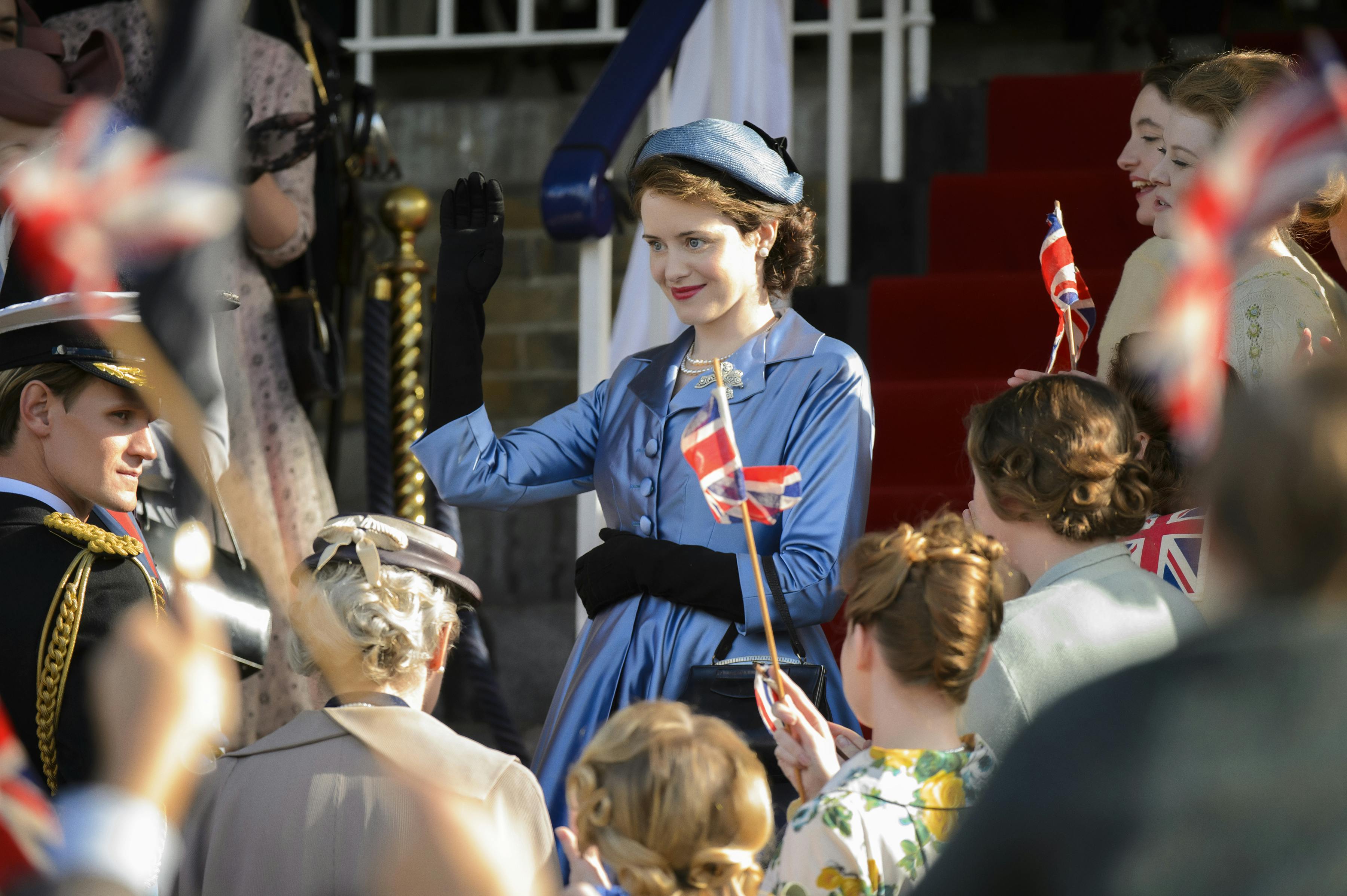 Queen Elizabeth (Claire Foy) wears a blue suit and embraces fans.