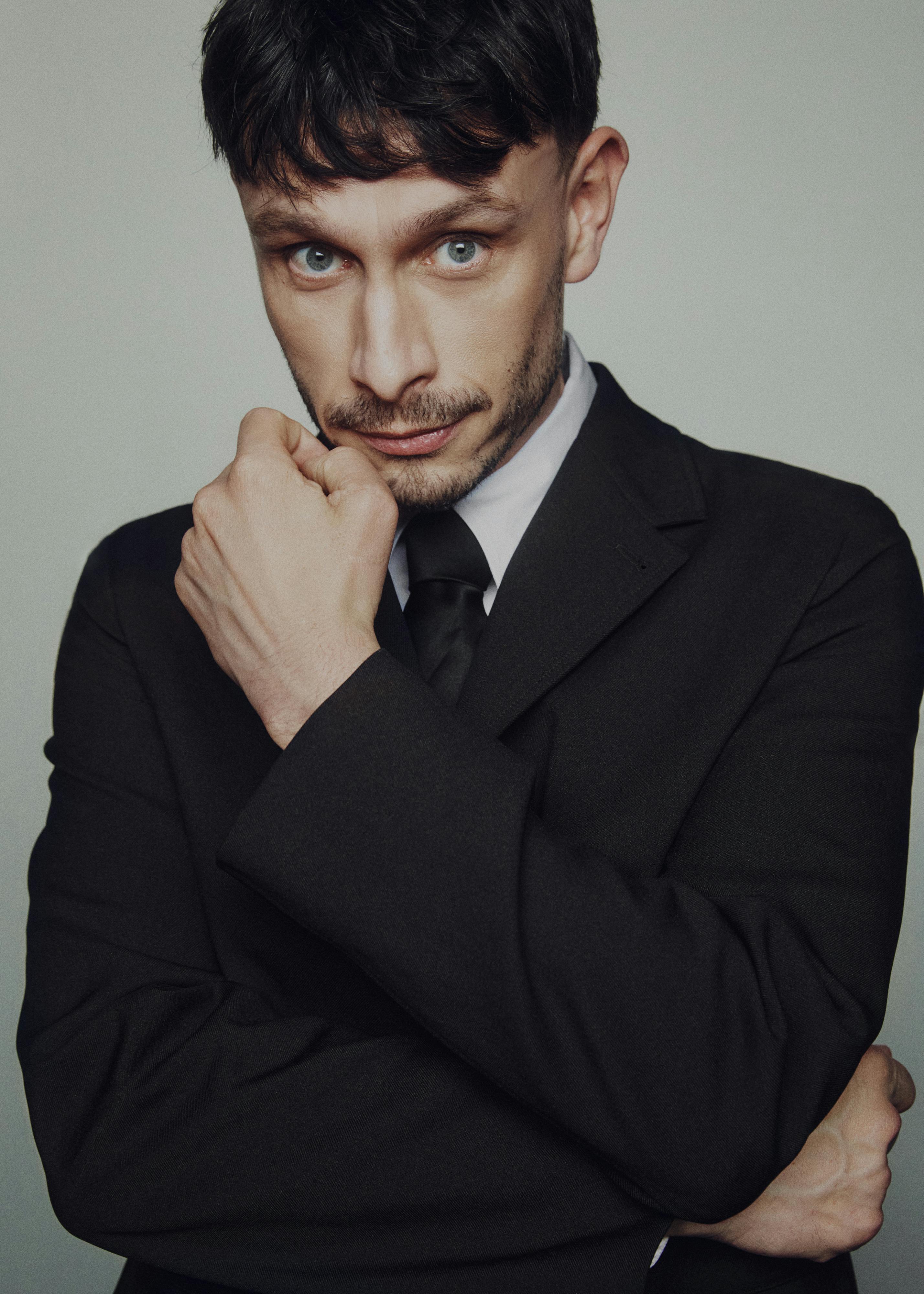 Richard Gadd wears a suit and poses with his finger on his mouth.