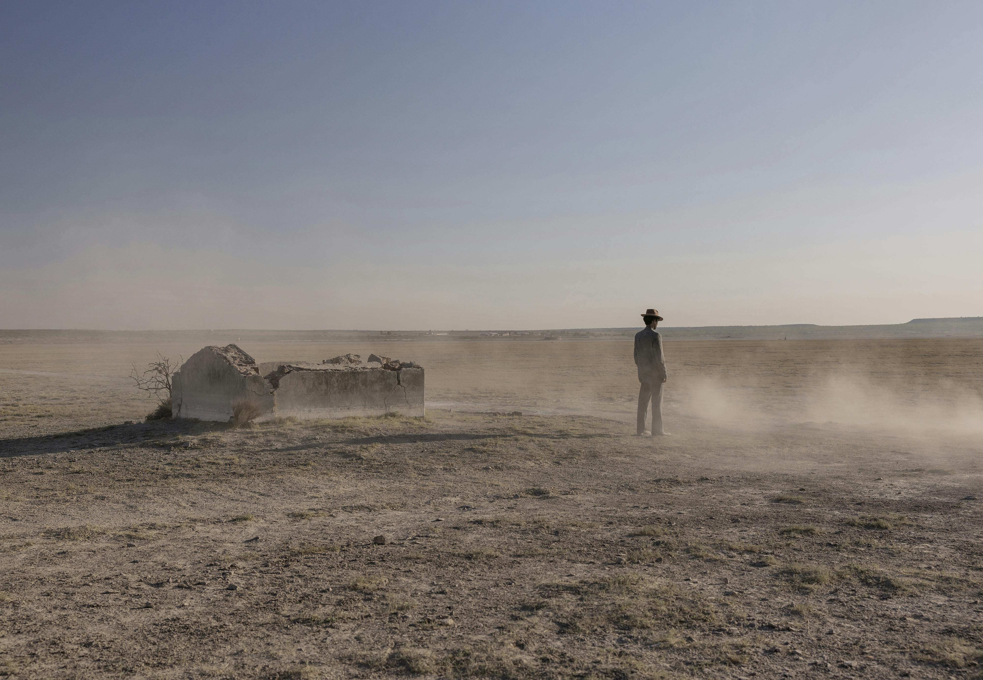 A figure stands in a cloud of dust in a deserted area, beneath a clear blue sky.