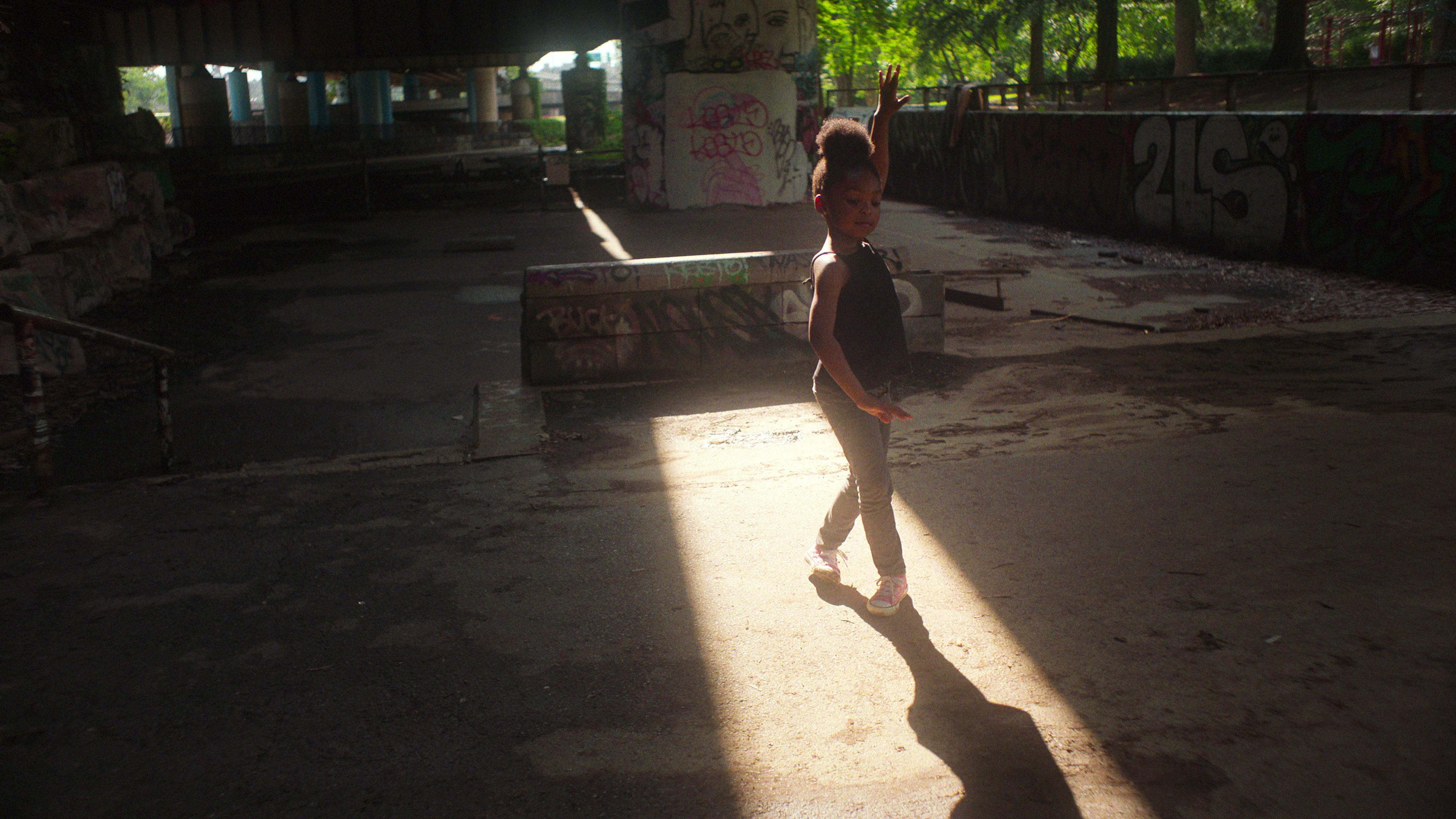 Aubrey Smith dances in a shaft of light, wearing pink converse.