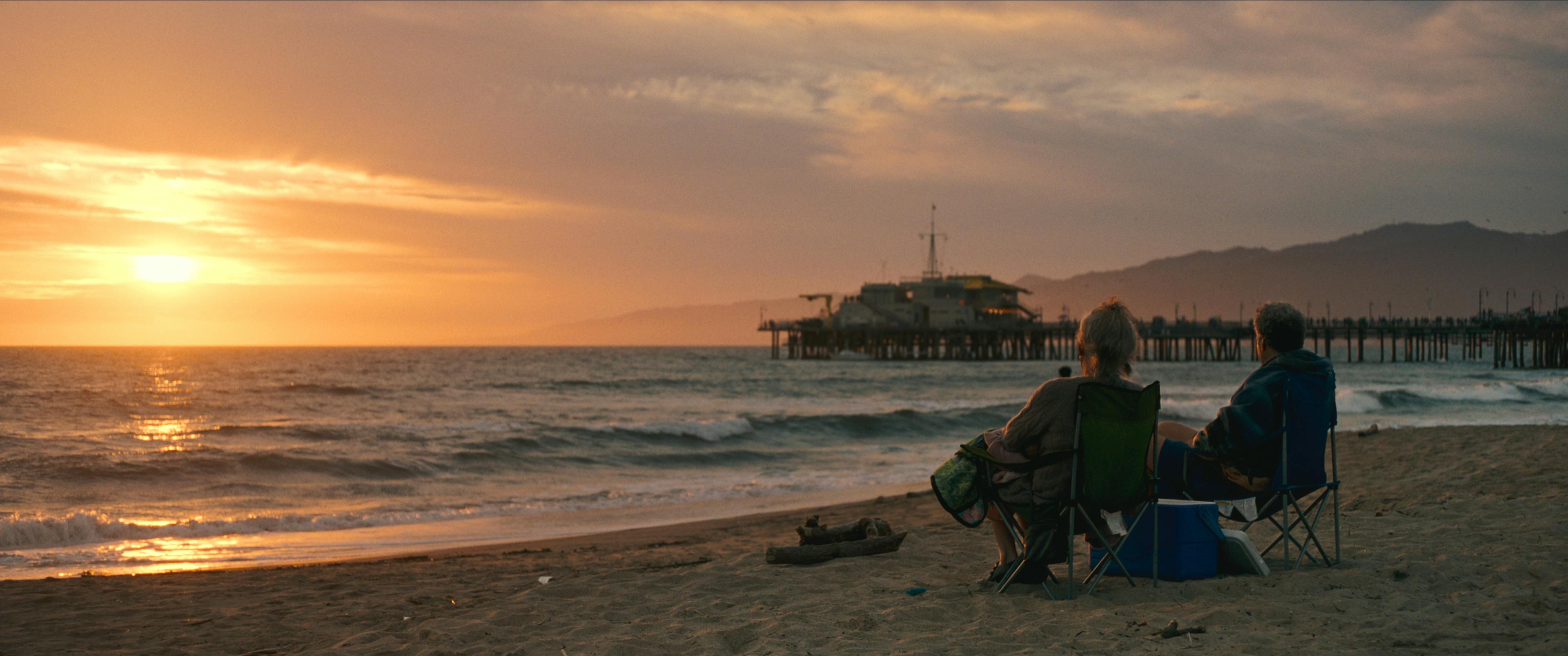 Will Ferrell and Harper Steele sit in beach chairs on the beach, the sun setting in the distance.