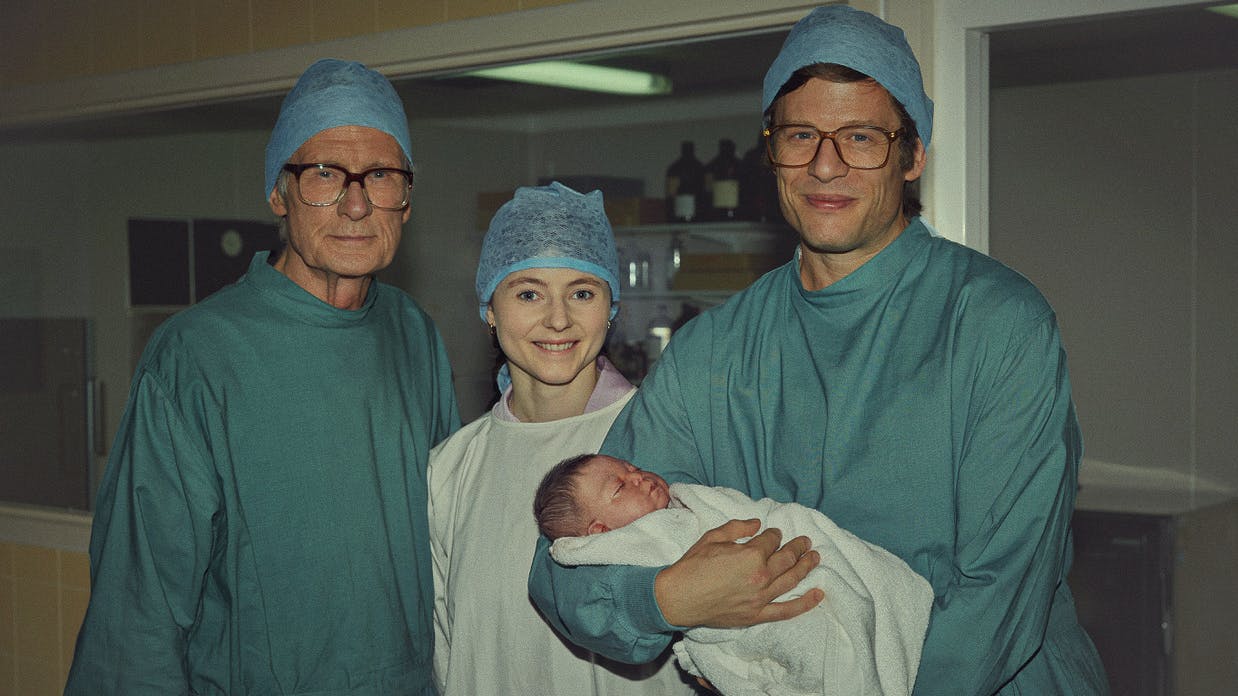 Patrick Steptoe (Bill Nighy), Jean Purdy (Thomasin McKenzie), and Robert Edwards (James Norton) wear scrubs and pose around a baby.