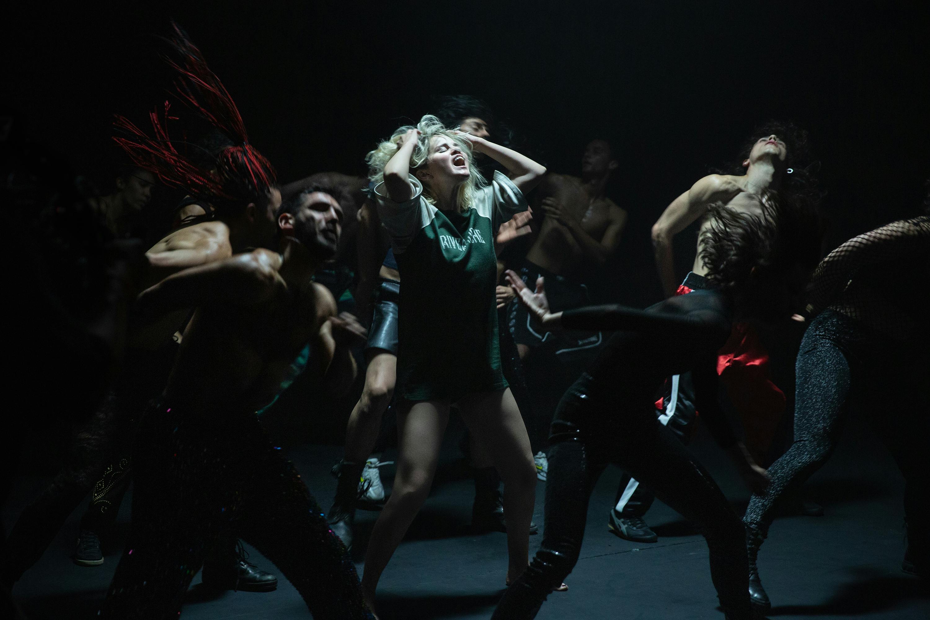 Scene from Emilia Pérez: Selena Gomez passionately performs "Bienvenida" surrounded by a cast of dancers. 