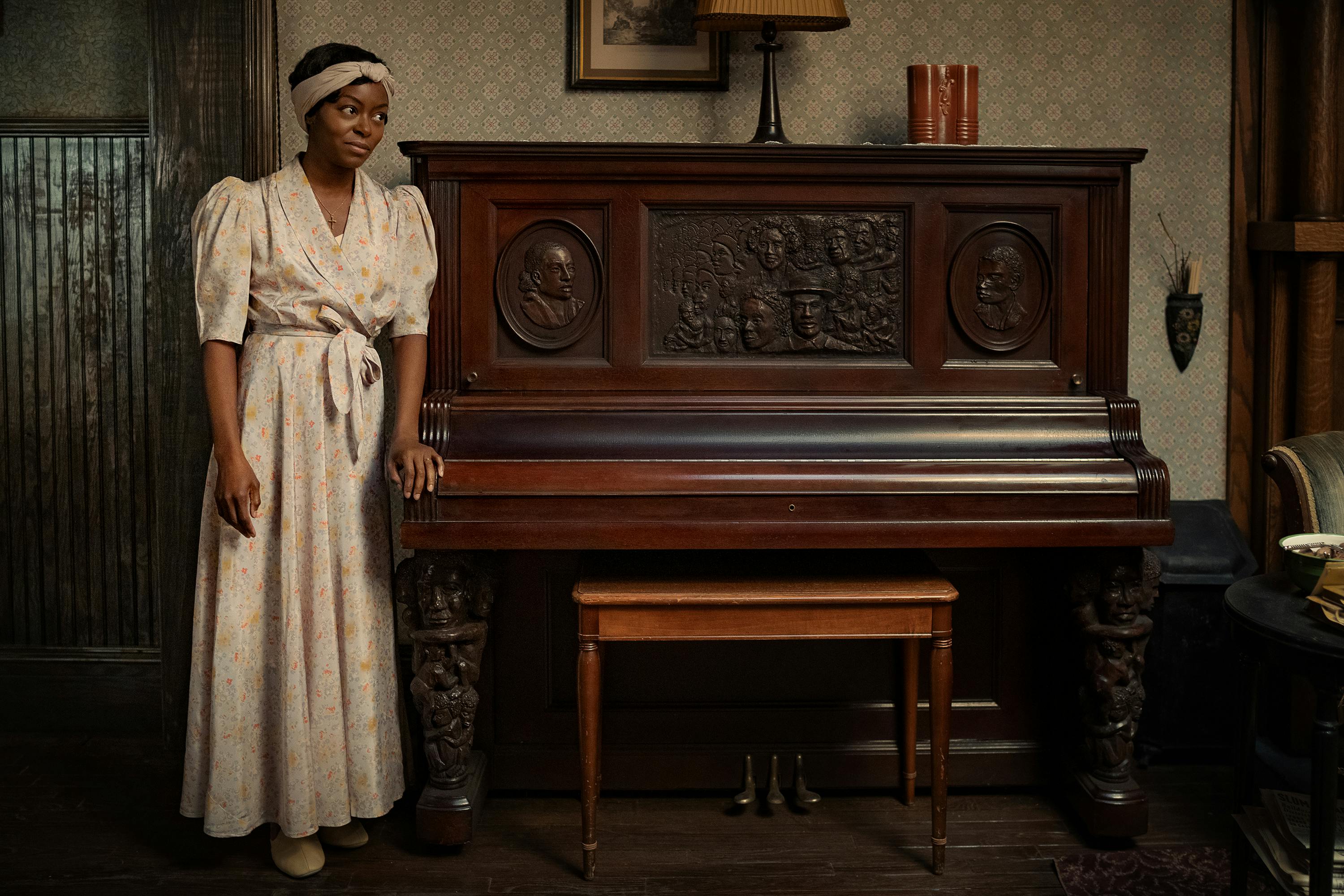 Berniece Charles (Danielle Deadwyler) stands in a white dress at an intricately carved wooden piano. 