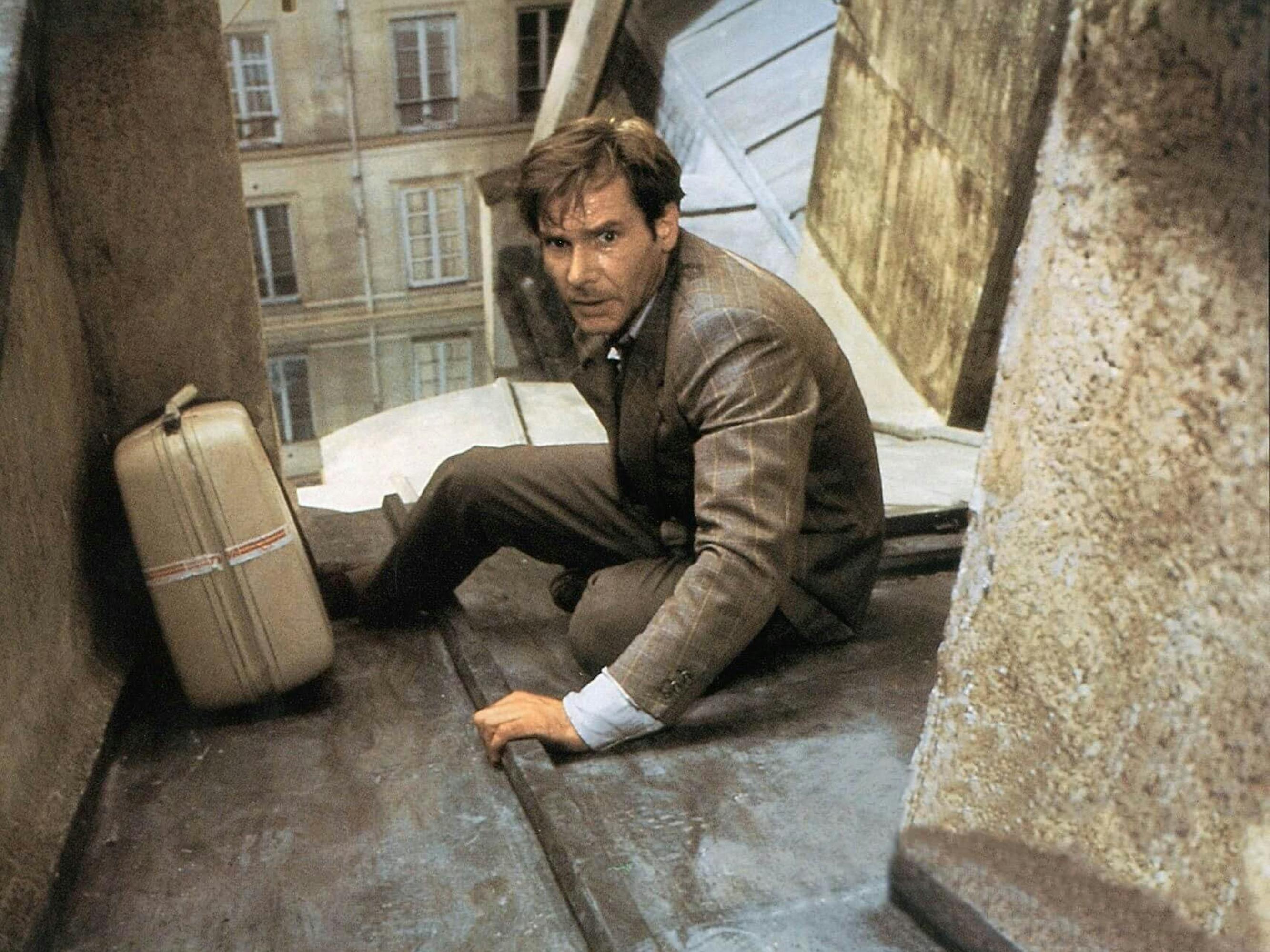 Dr. Richard Walker (Harrison Ford) in Frantic. He wears a brown suit and scales a roof with a briefcase.