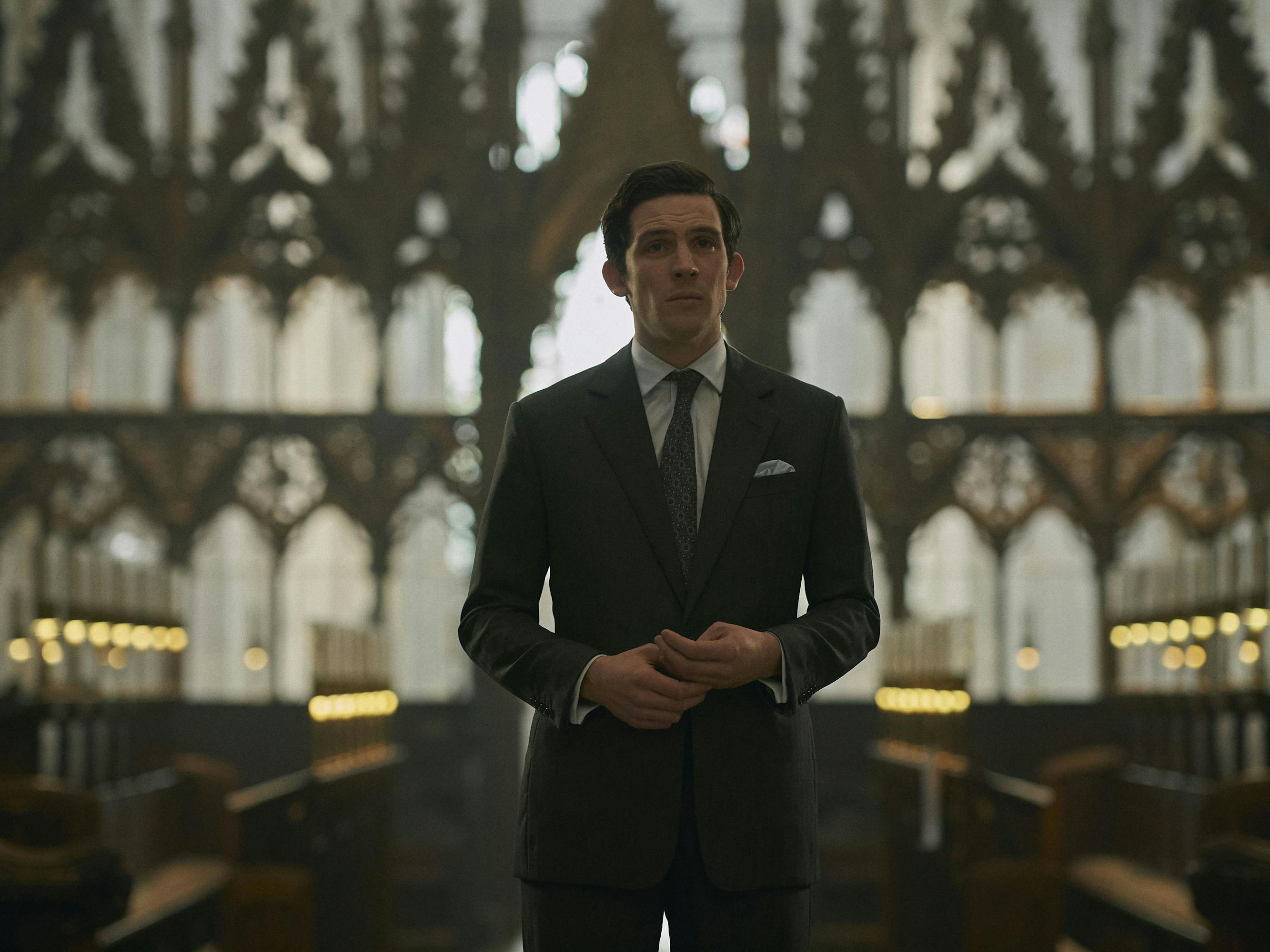 Prince Charles (Josh O'Connor) wears a suit and stands in a drafty church looking daunting.