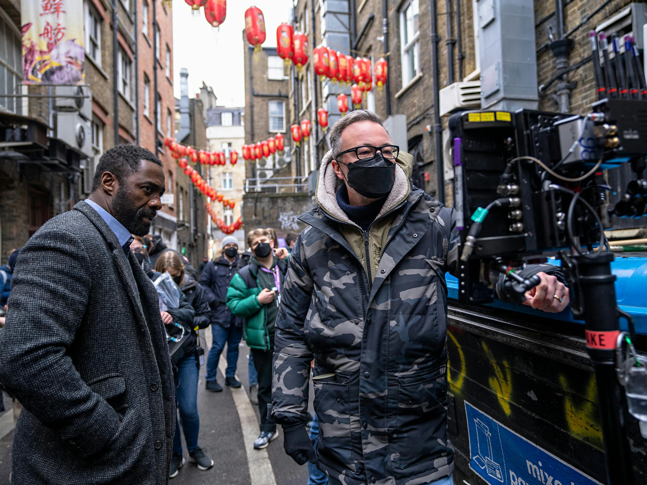 Idris Elba and James Payne behind the scenes, on a busy, narrow street.