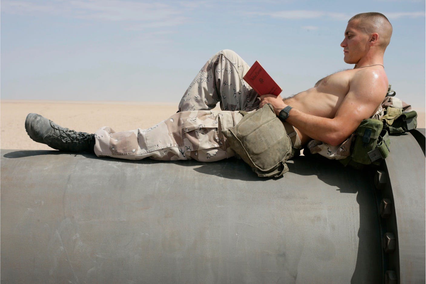 Anthony Swofford (Jack Gyllenhaal) in Jarhead (2005) sits on an army tanker. The profile view gives us a great view of his biceps muscles. He wears no shirt, khaki cargos, and reads a red book.