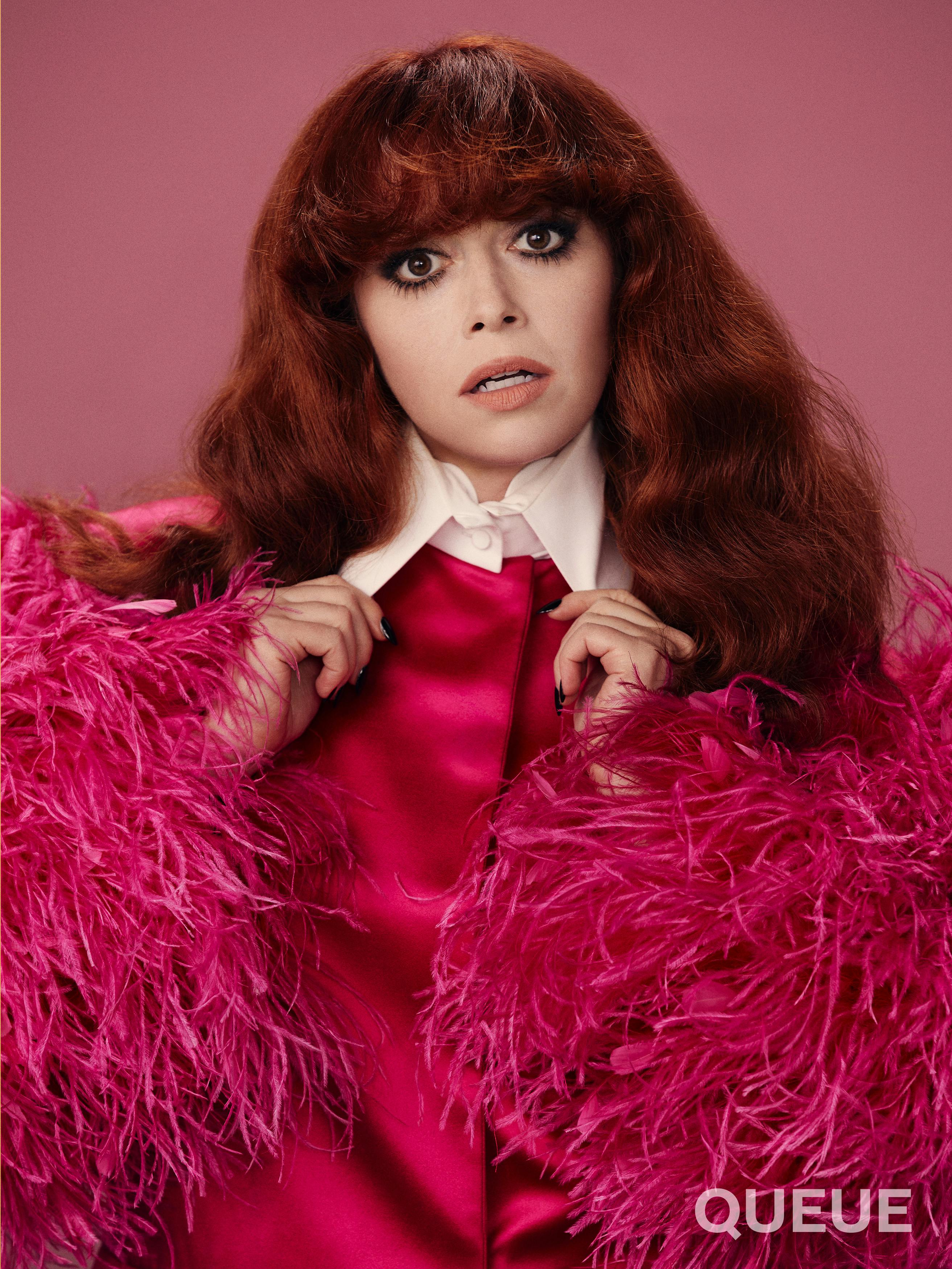 Natasha Lyonne wears a pink top with feathered sleeves, and a dramatic white collar.