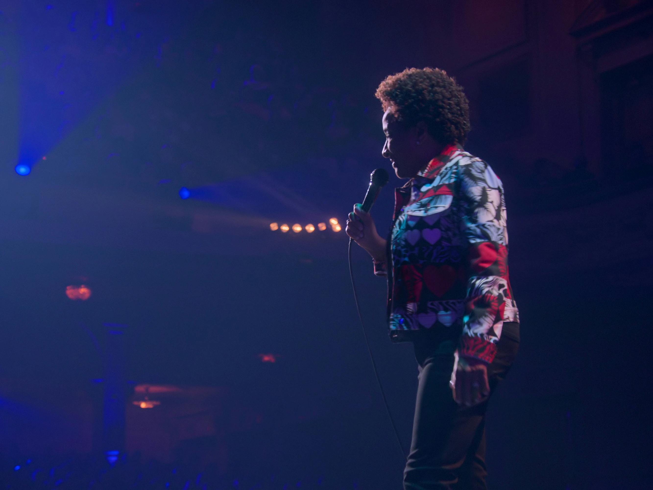 Wanda Sykes wears a patterned suit and stands on a foggy stage. 