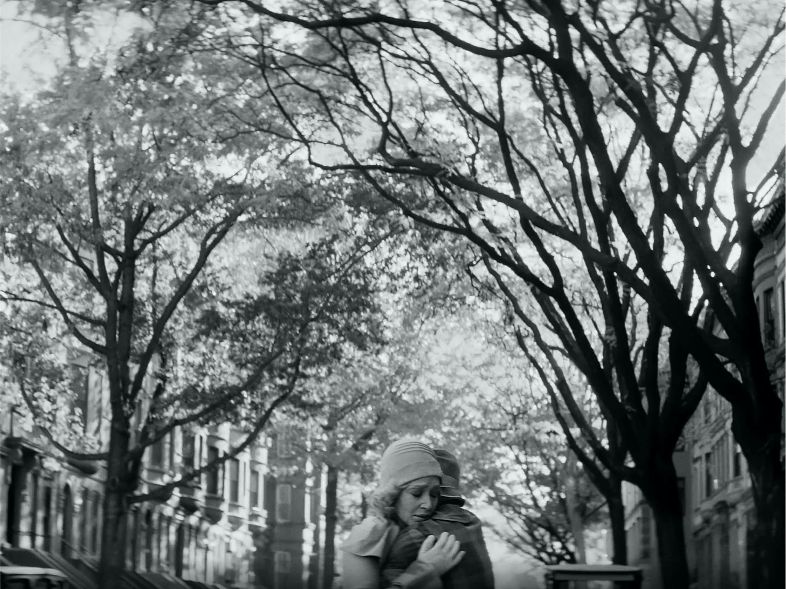 Clare (Ruth Negga) and Irene (Tessa Thompson) embrace in the middle of a tree-lined street, framed by brownstones.
