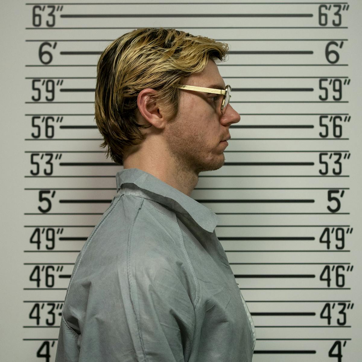Jeffrey Dahmer (Evan Peters) stands in profile in front of a wall getting his mugshot taken.