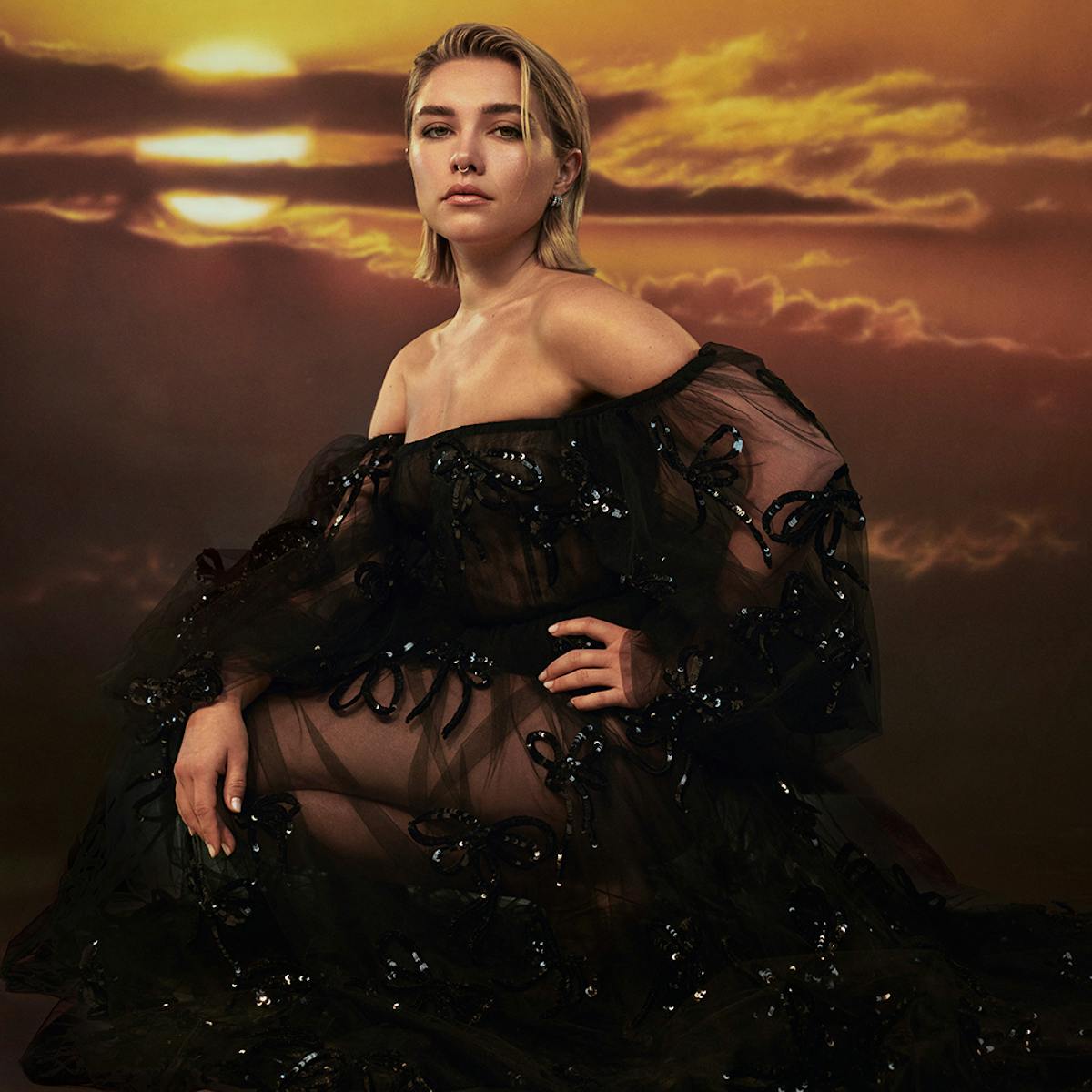 Florence Pugh wears a black sequin sheer dress and stands in front of a a bright yellow sun.