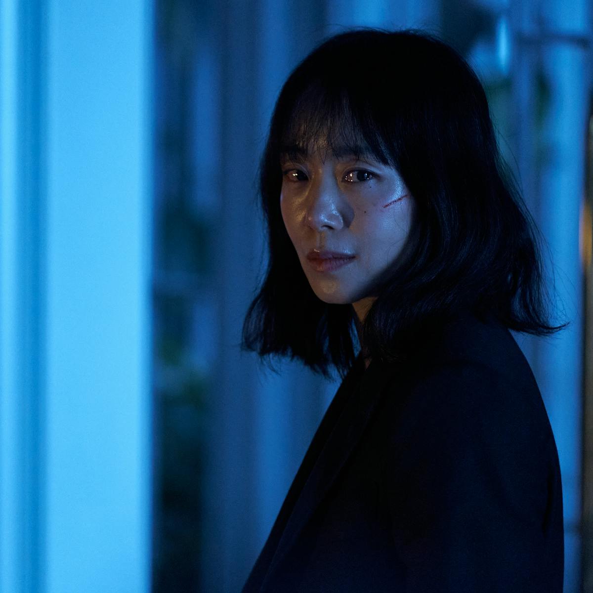 Jeon Do-yeon wears a black top and looks at the camera. On her cheek is a thin red cut. 