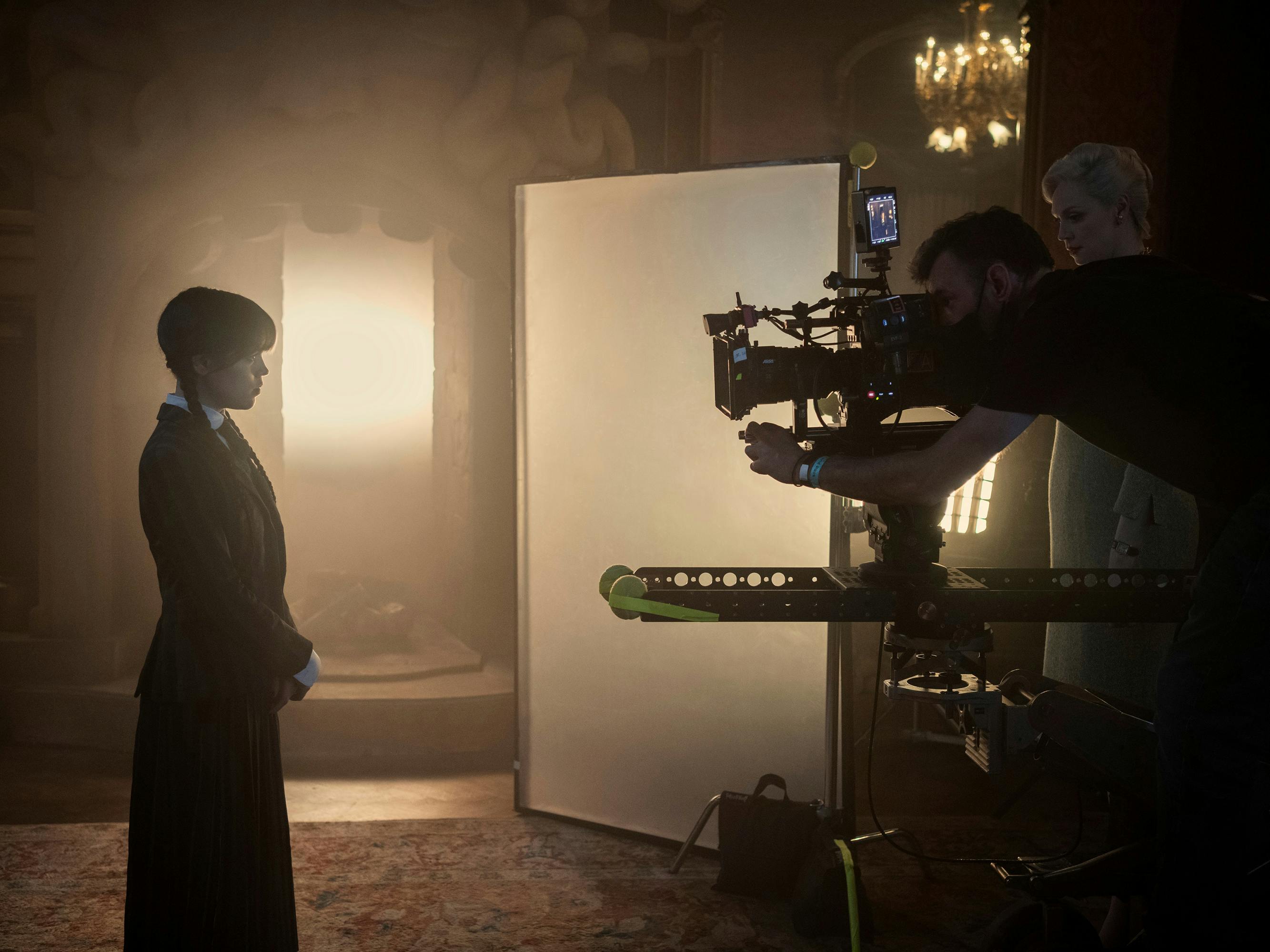 Wednesday (Jenna Ortega) behind the scenes, in a dimly-lit shot.