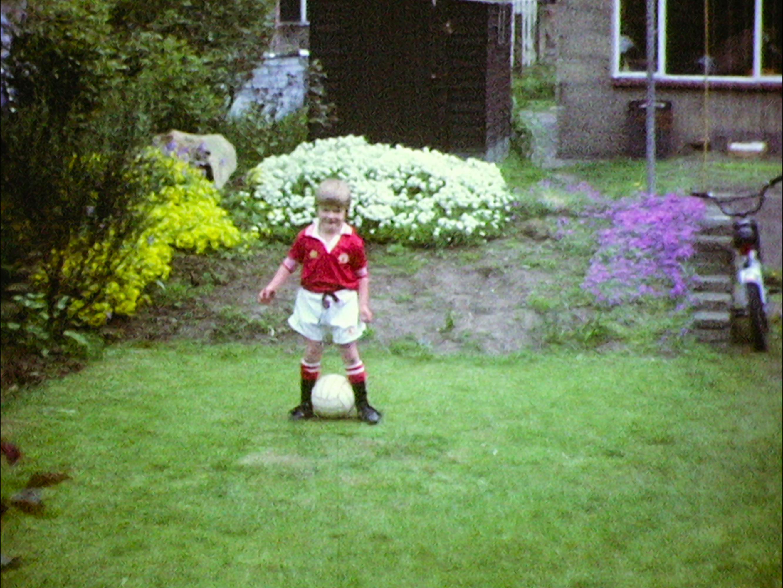 A young David Beckham kicks a ball around a grassy backyard.