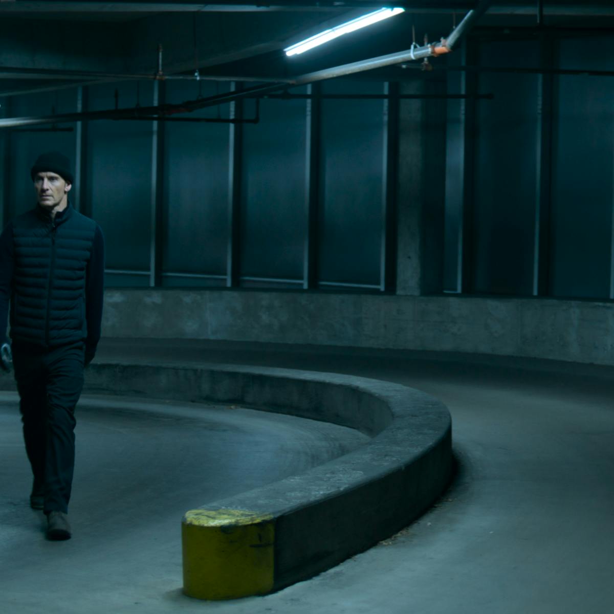 The Killer (Michael Fassbender) wears a black ensemble and walks through a parking garage. Scary!