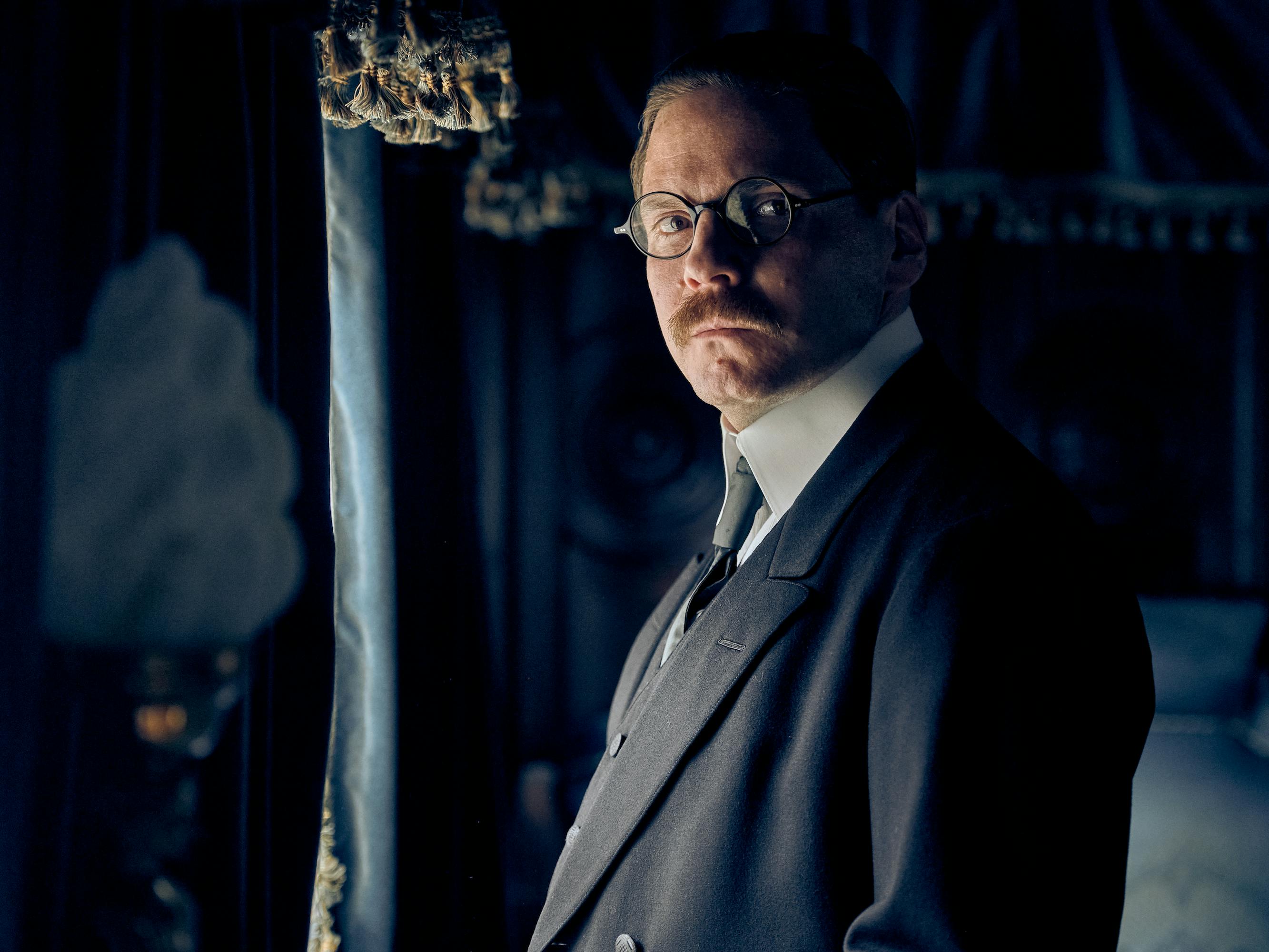 Matthias Erzberger (Daniel Brühl) wears a dark suit and glasses and has an impressive mustache in this dark picture.