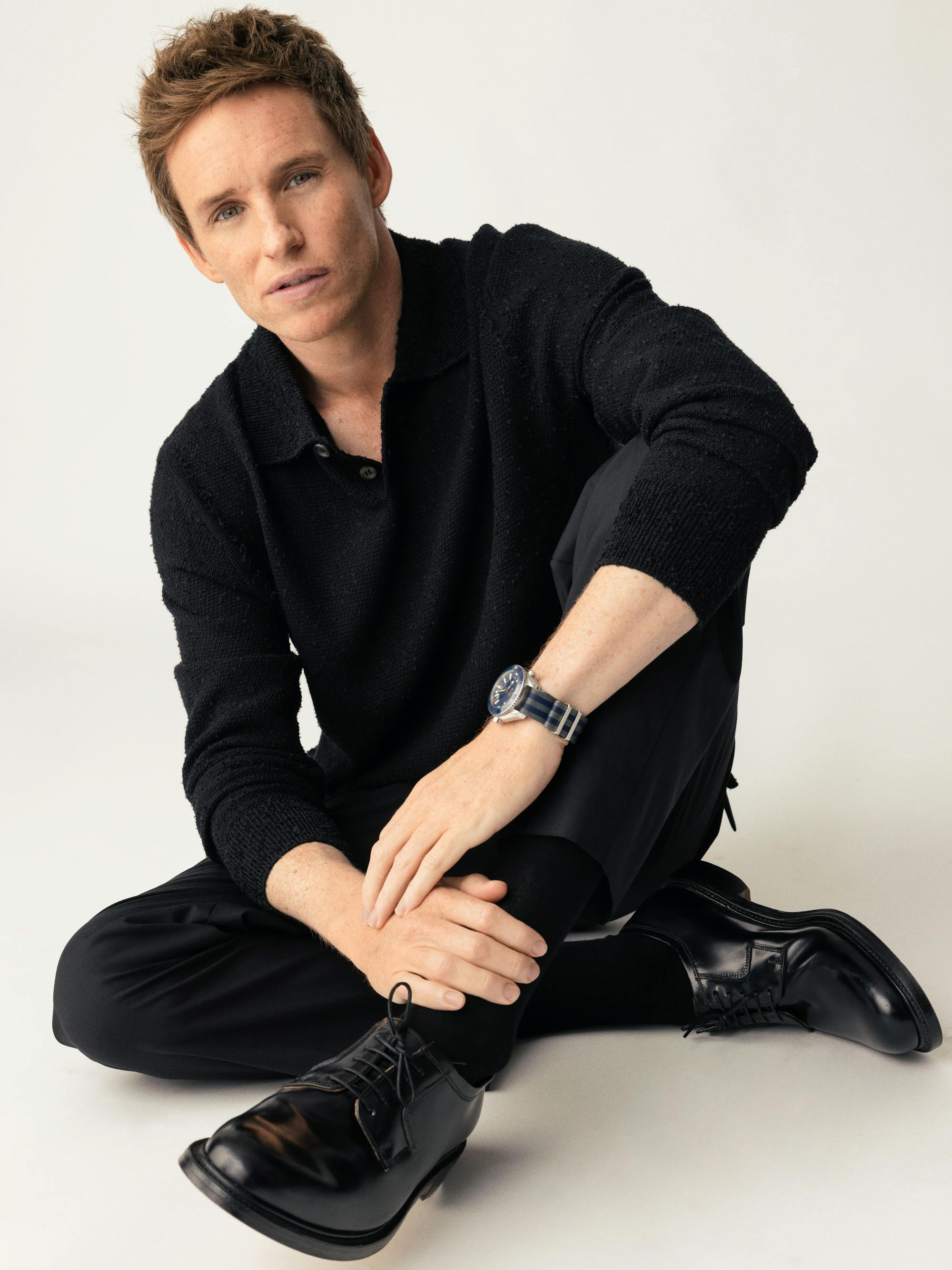 Eddie Redmayne on a digital cover of Queue wearing a black ensemble, shoes, and a black watch.