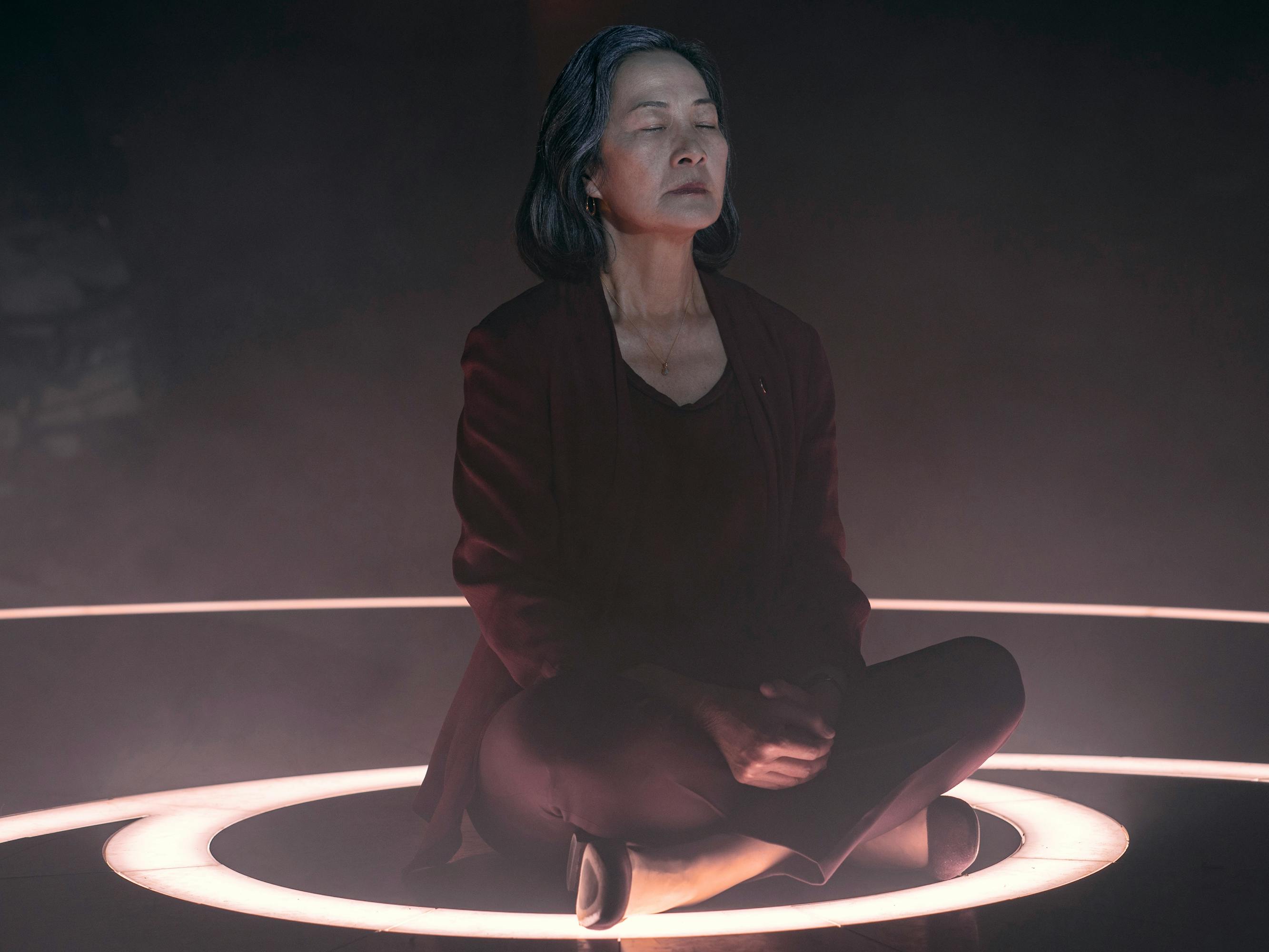 Ye Wenjie (Rosalind Chao) sits on a circle of light, with her legs crossed and eyes closed.