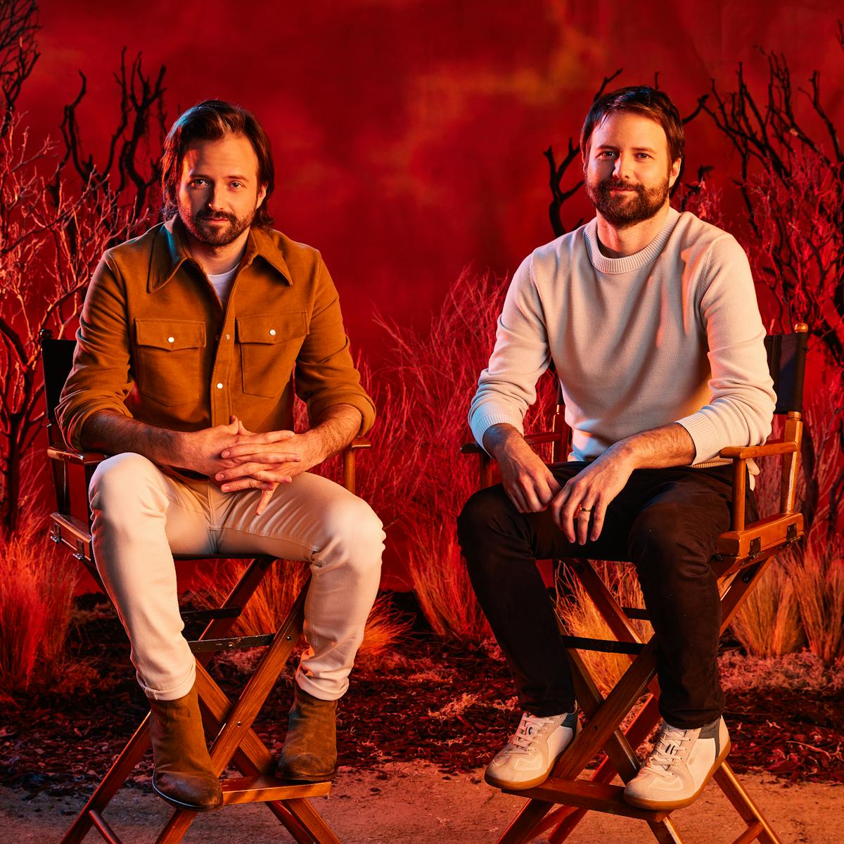 Matt and Ross Duffer sit in directors chairs against a fiery red backdrop.