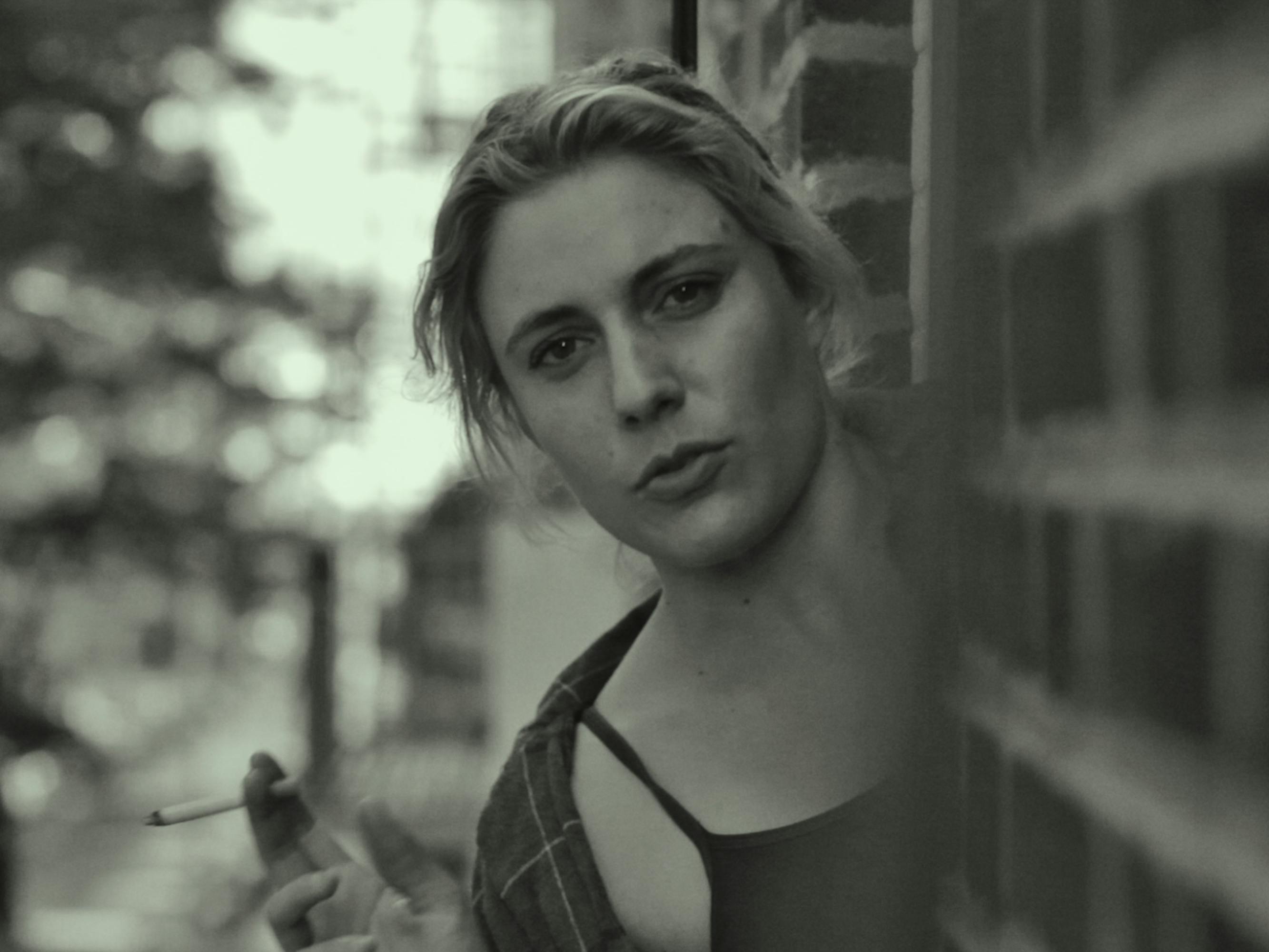 Frances (Greta Gerwig) looks from behind a wall directly at the camera.