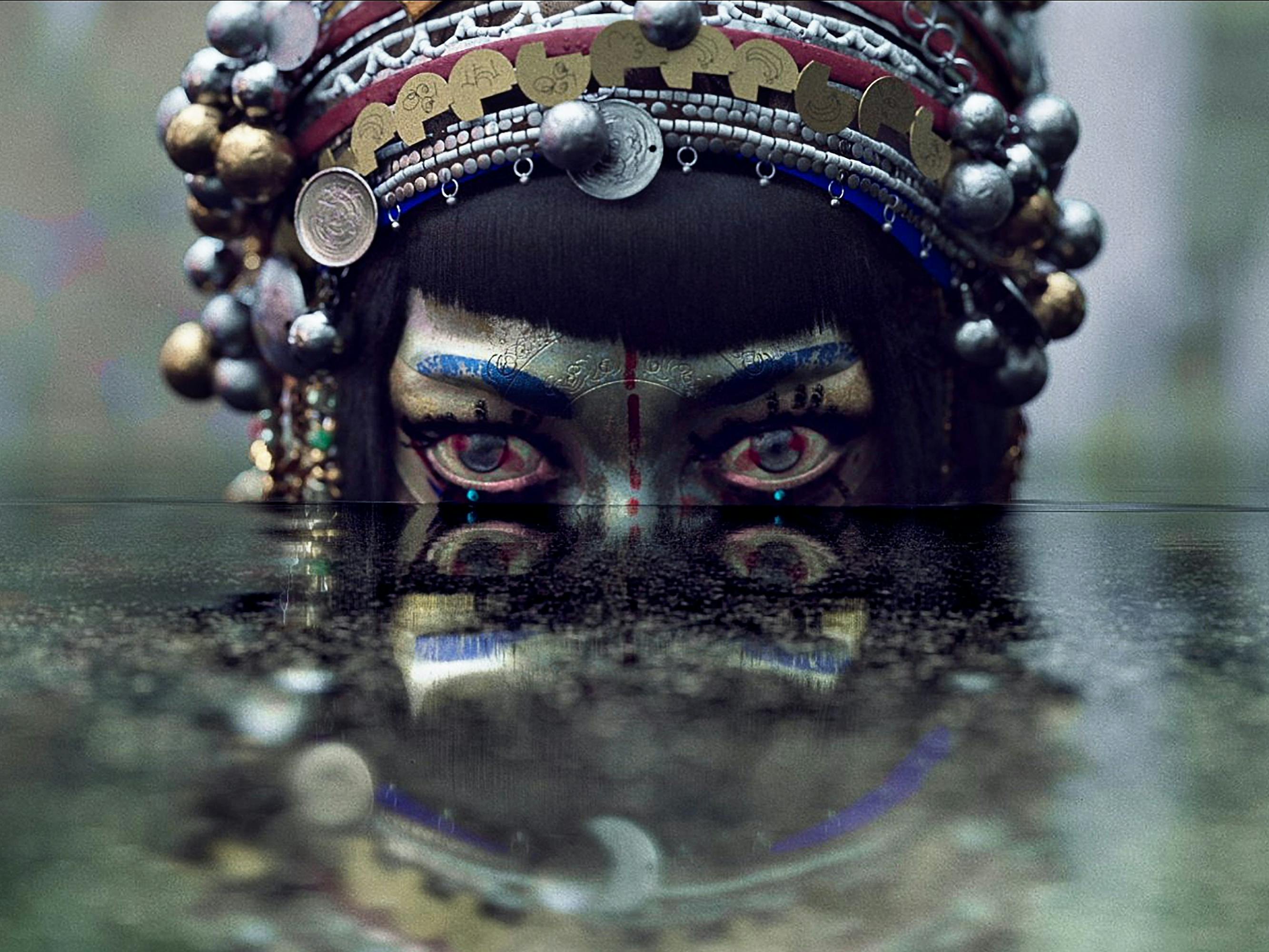 We see half the siren's face; the rest is obscured by water. Her head is adorned with beads and a headdress. 