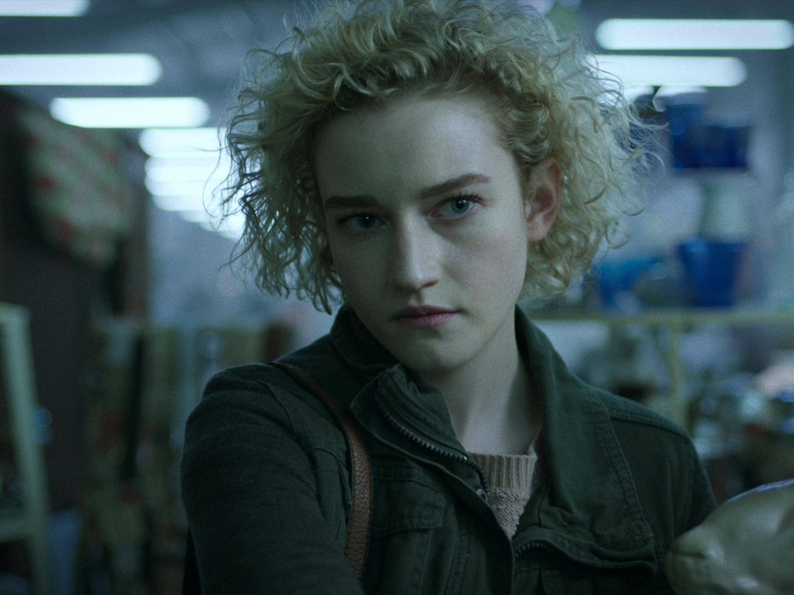 Julia Garner has curly blond hair and wears a green jacket.